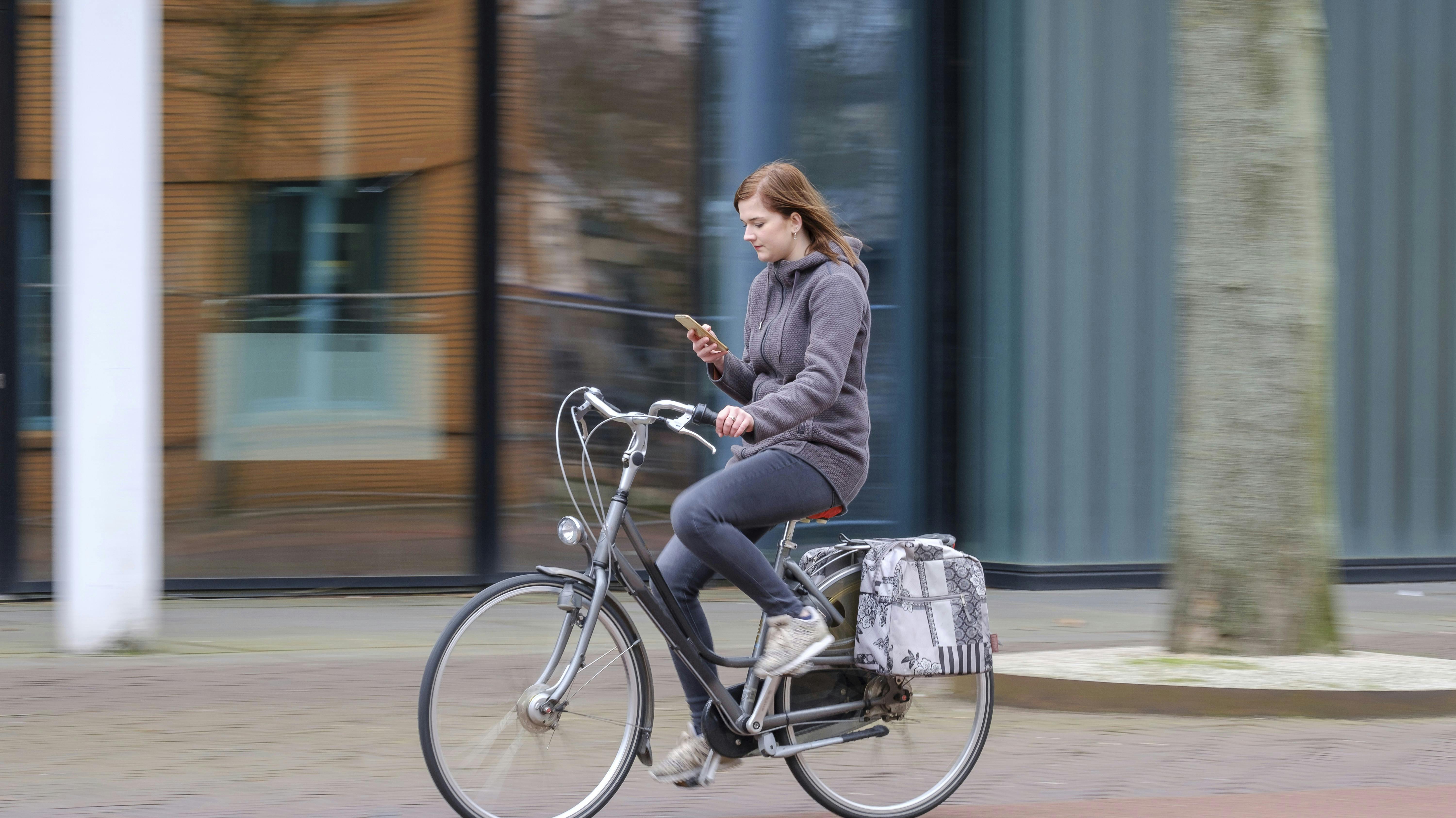 Young woman getting distracted by his smartphone while riding his bicycle around the city