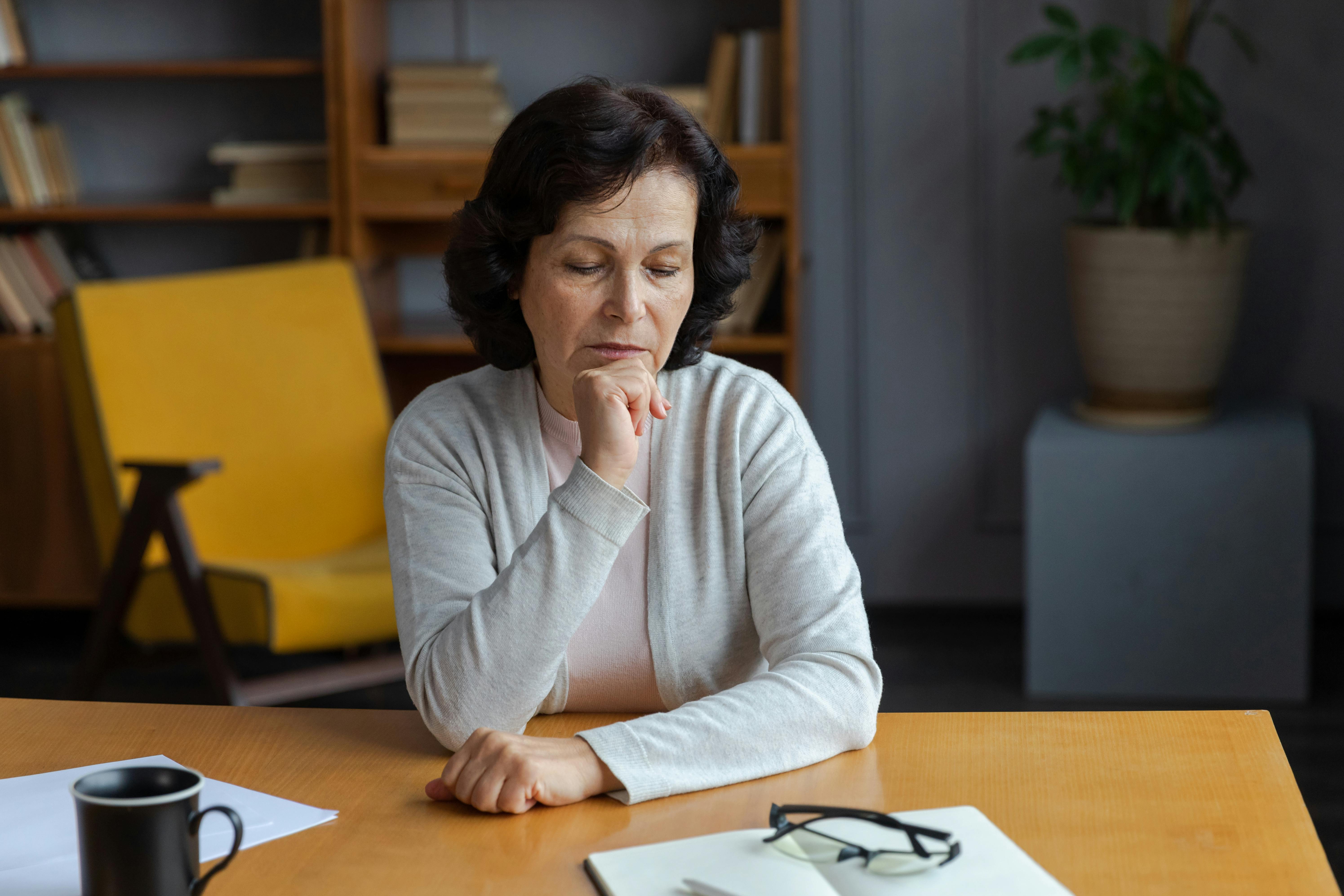 Ældre kvinde sidder alene ved sit spisebord og ser trist og ensom ud.