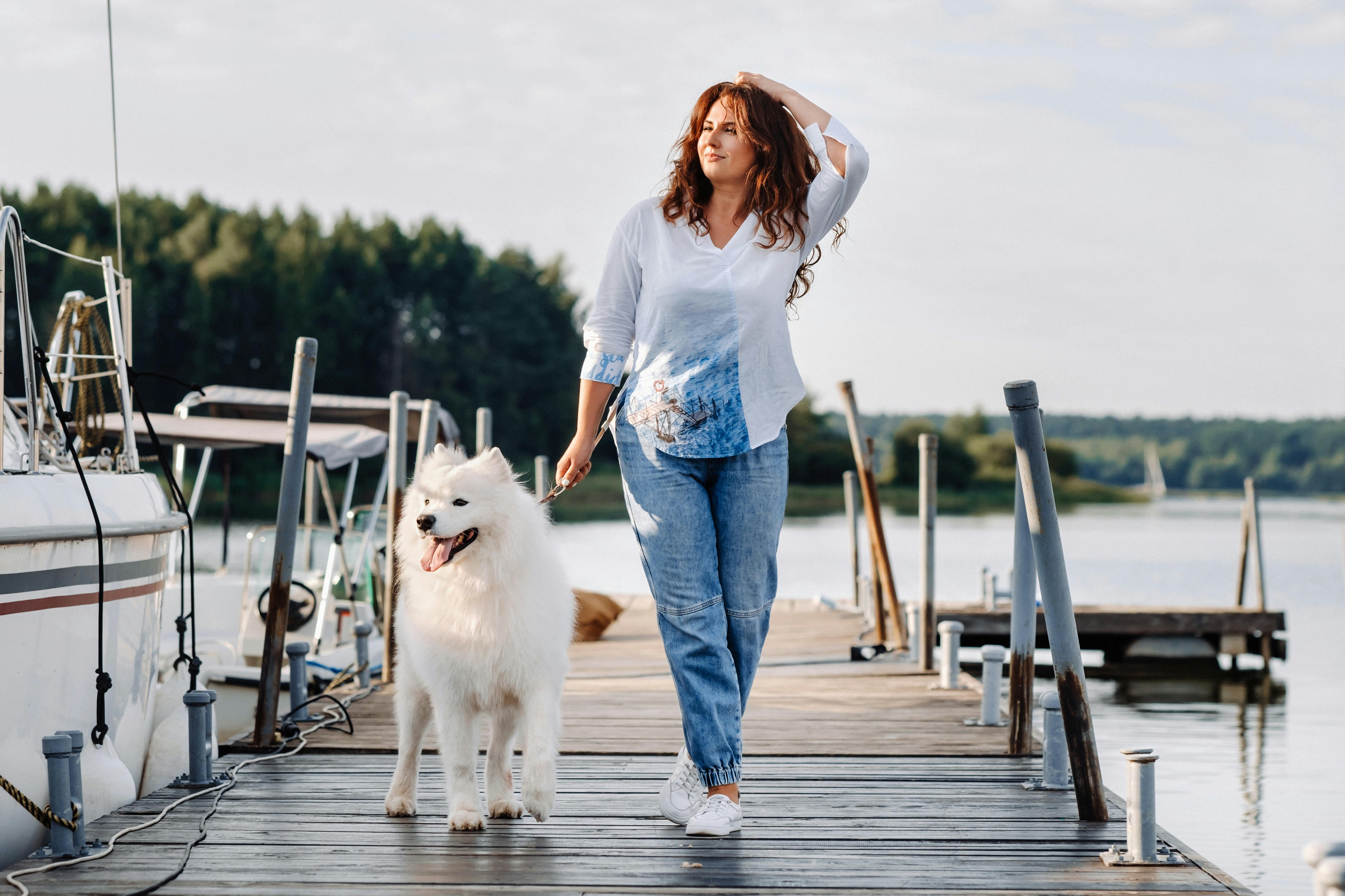 Kvinde lufter sin hund på bådbroen ved en lystbådehavn.