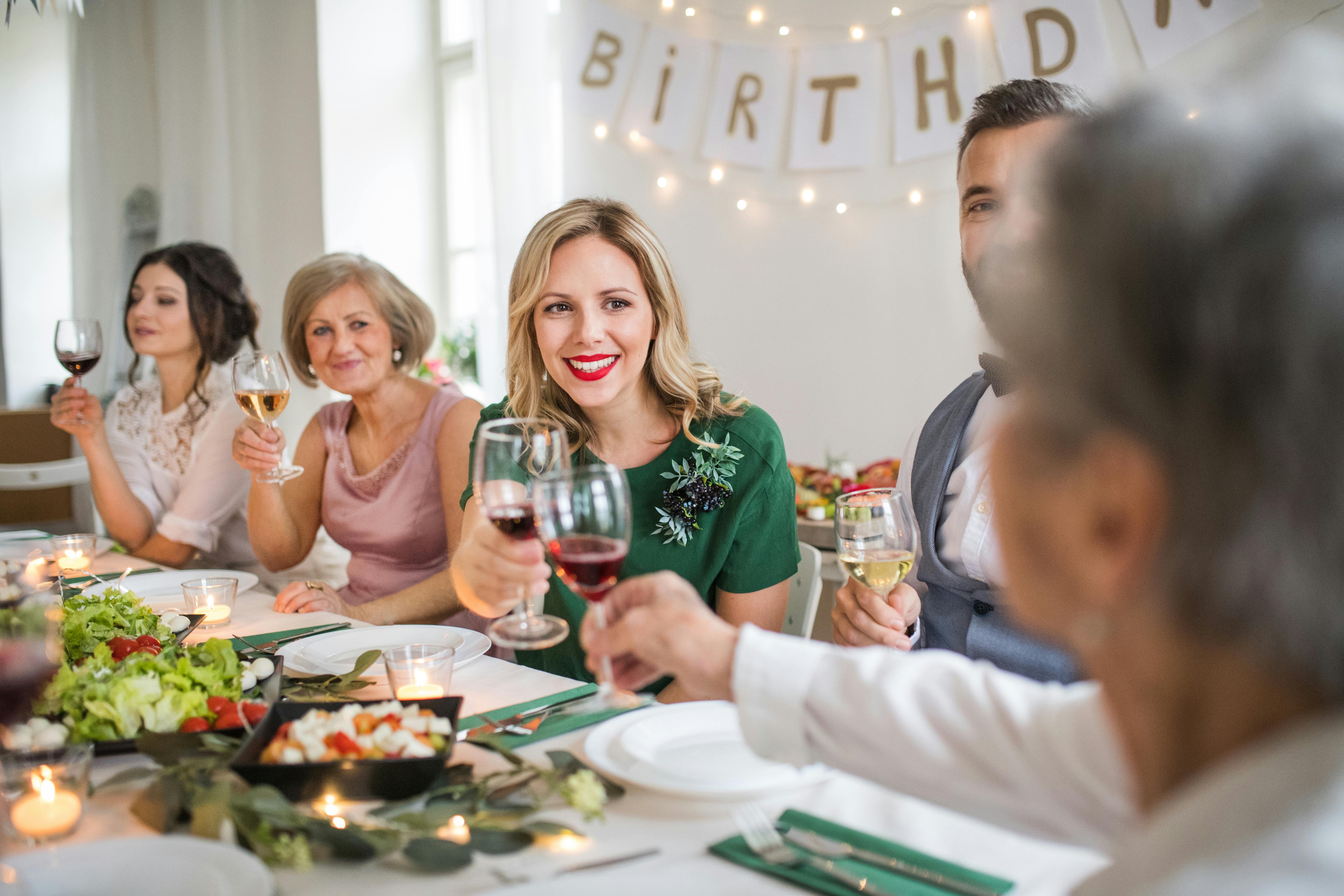 Familie sidder til bords ved fødselsdagsfest, hvor en ældre kvinde ser skeptisk på et par, der skåler.