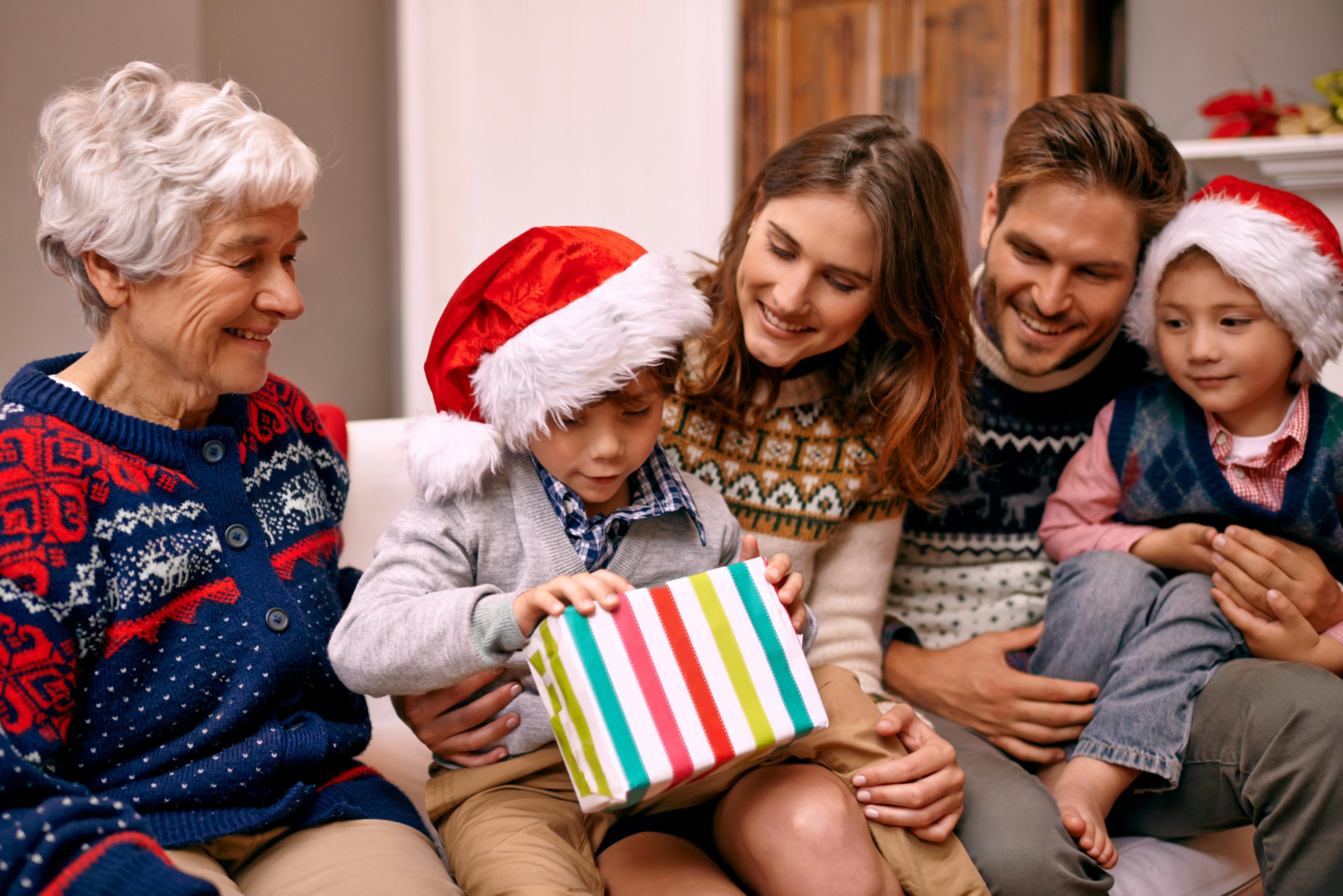 Mor, far og bedstemor ser spændt til, mens en dreng åbner sin julegave. Et andet barn sidder uden en pakke og ser trist ud., mens et andet barn ser trist