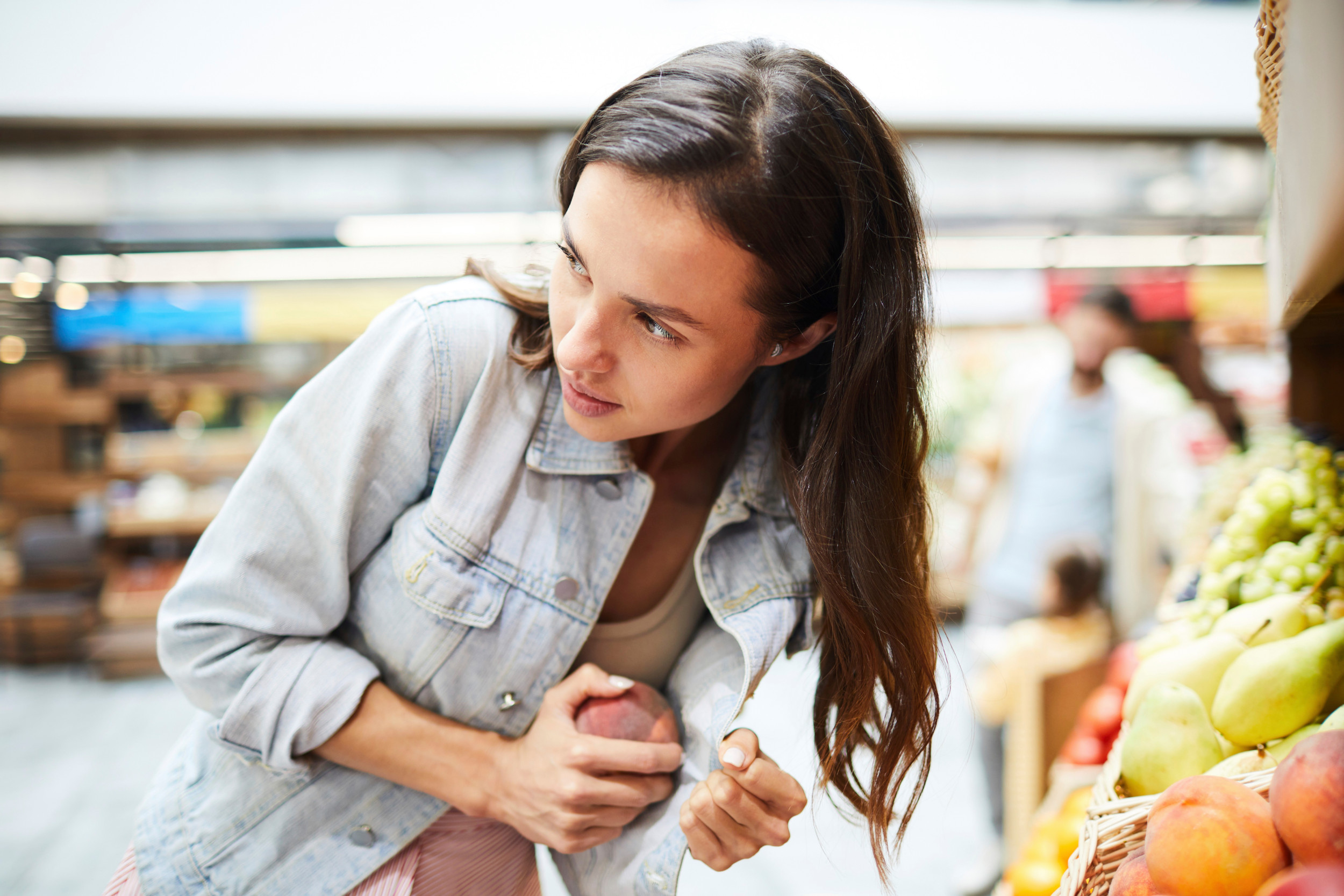 Ung kvinde i supermarked gemmer en frugt under sin jakke.