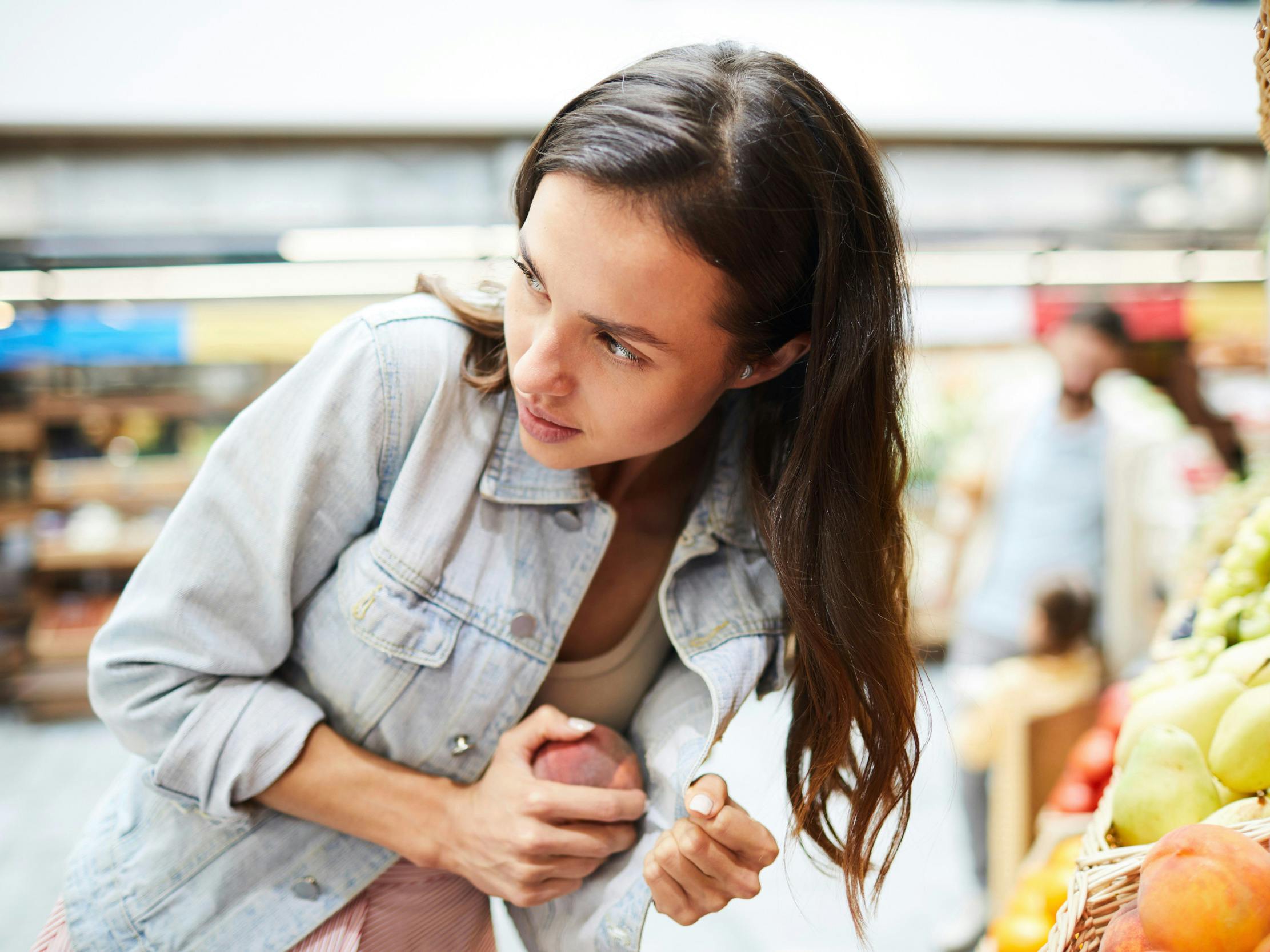 Ung kvinde i supermarked gemmer en frugt under sin jakke.
