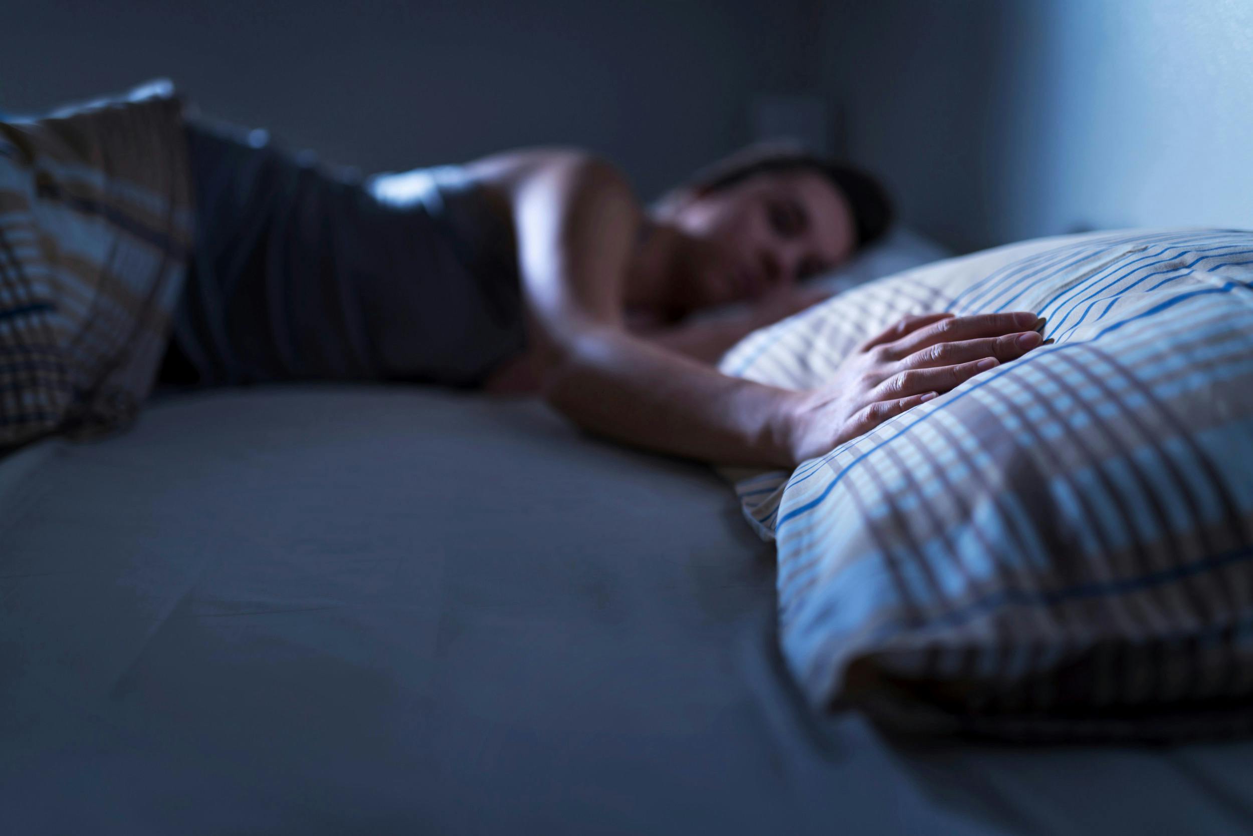 Sovende kvinde lægger hånden på den tomme pude ved hendes side.
