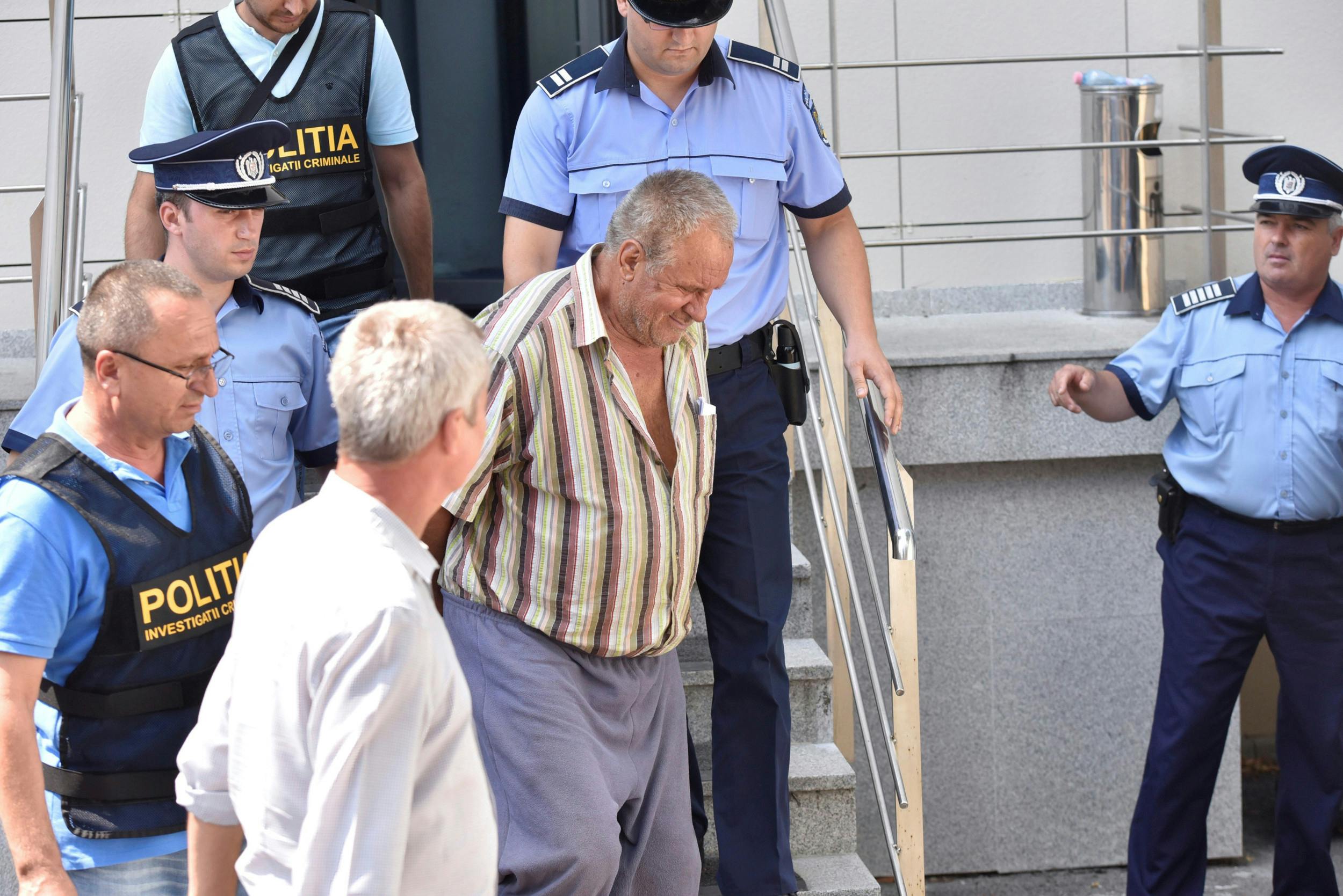 Den 65-årige Gheorghe Dinca eskorteres ud af retten i Craiova, Rumænien.