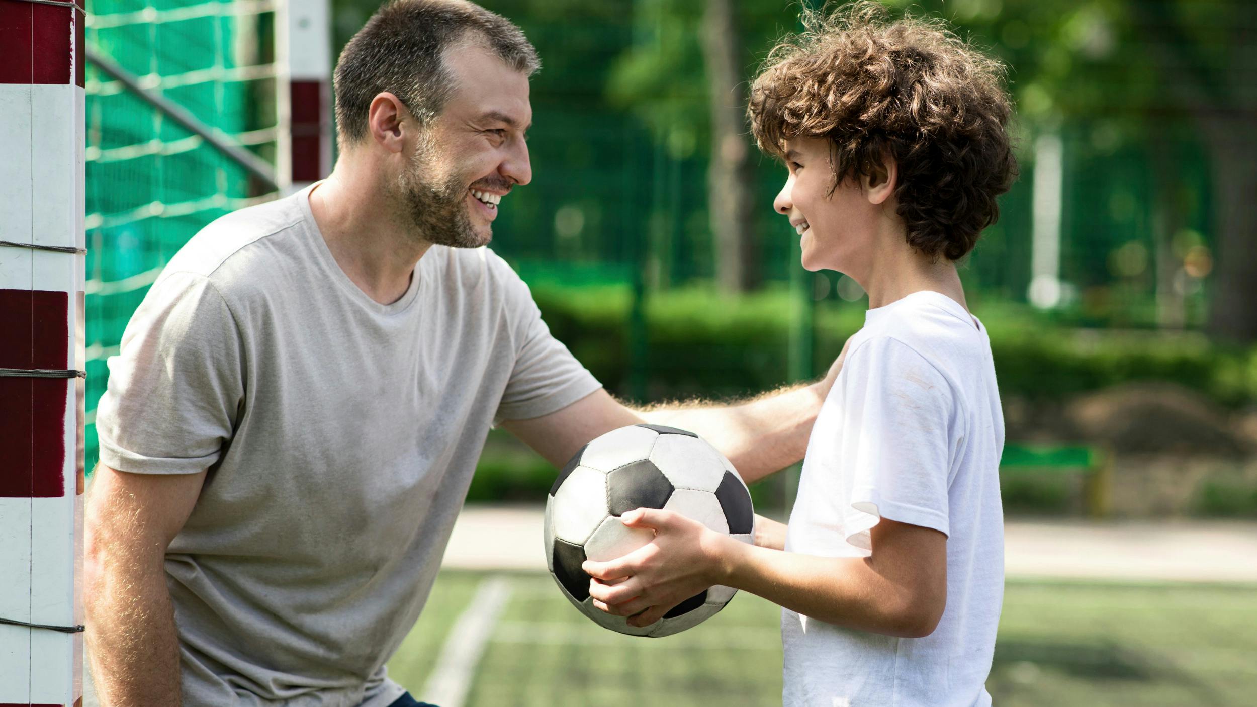Far ser smilende på sin søn, der holder en fodbold.
