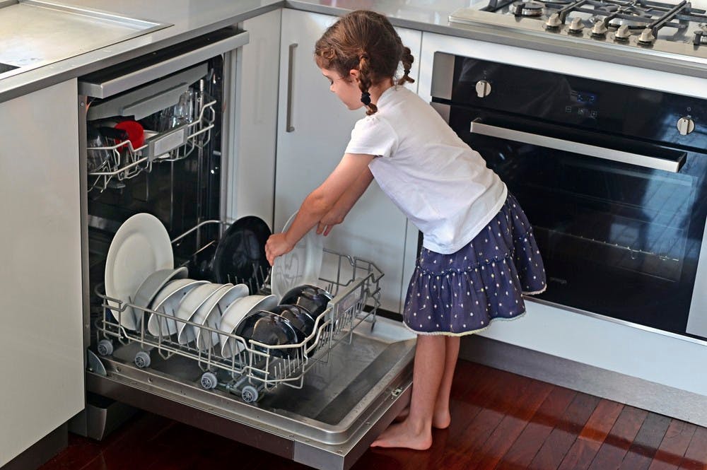 Lille pige fylder tallerkener i opvaskemaskinen.