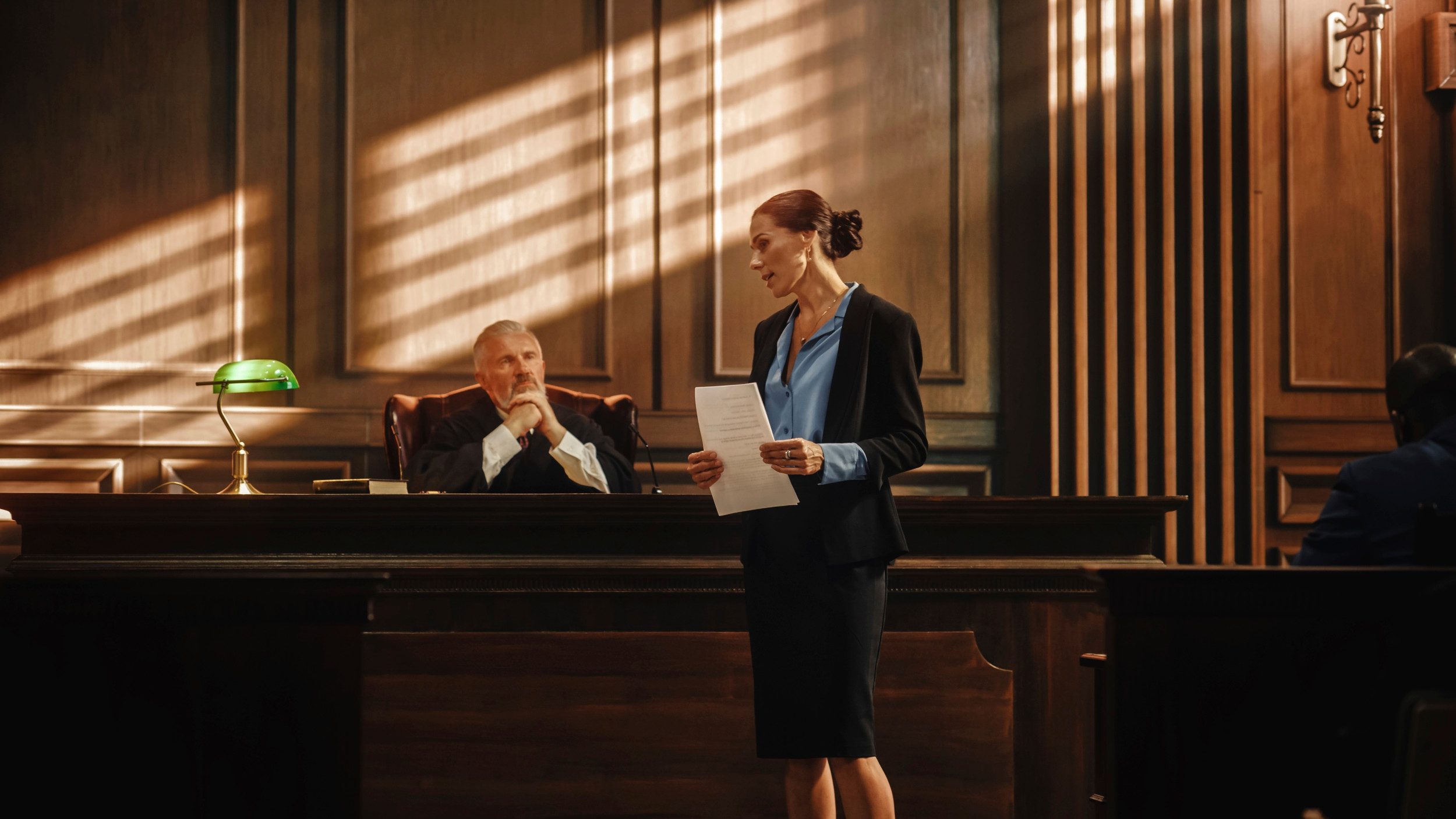 En kvindelig advokat står og taler foran en mandlig dommer, der sidder og lytter