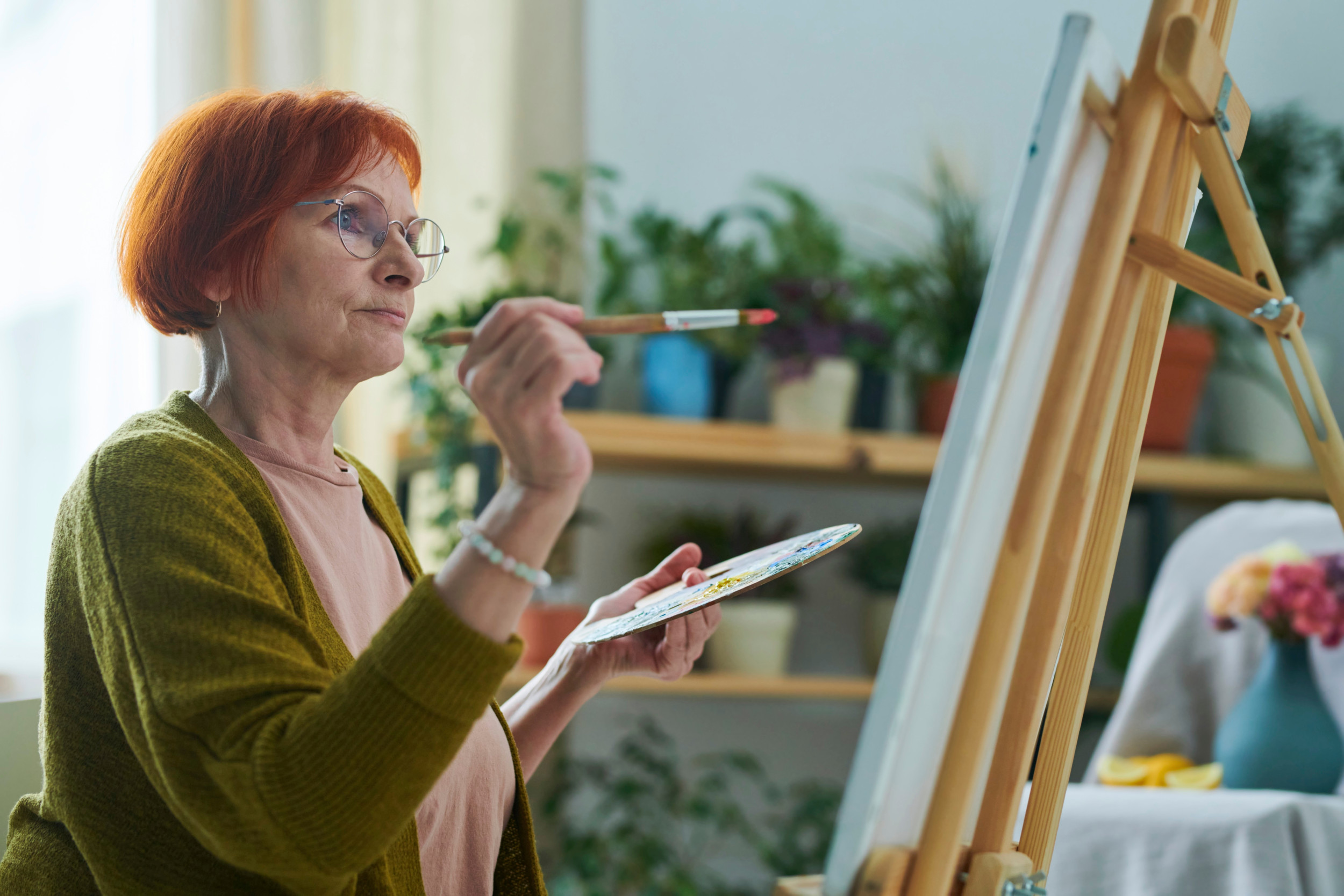 Midaldrende kvinde står ved et staffeli og maler koncentreret.