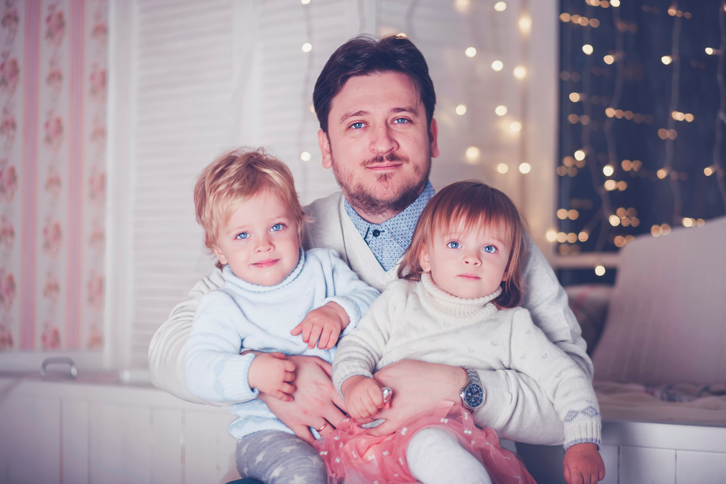 Ung far sidder med sine 2-årige tvillinger i favnen.