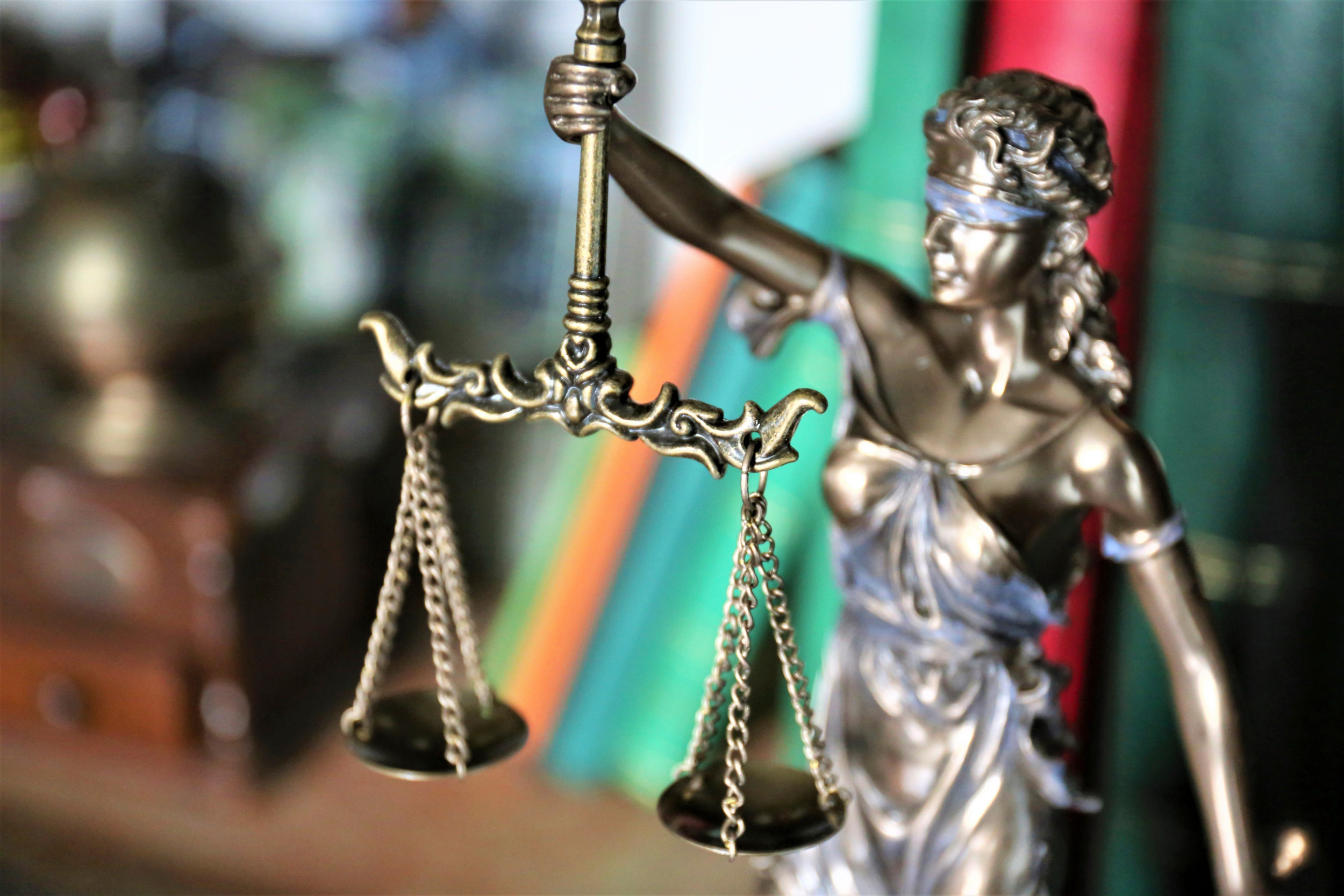 Retfærdighedens gudine holder sin vægt frem. Figuren står foran en række bøger.