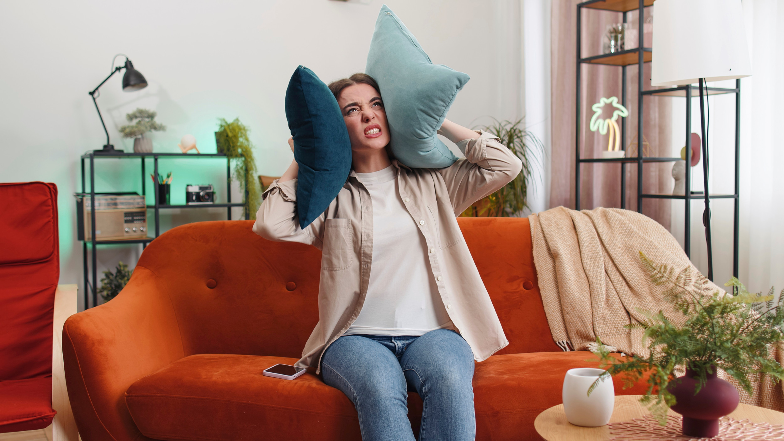 Kvinde sidder i sin sofa med en pude for hvert øre, fordi overboen larmer.