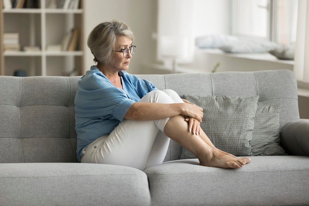 Midaldrende kvinde sidder alene på sin sofa og ser trist ud.