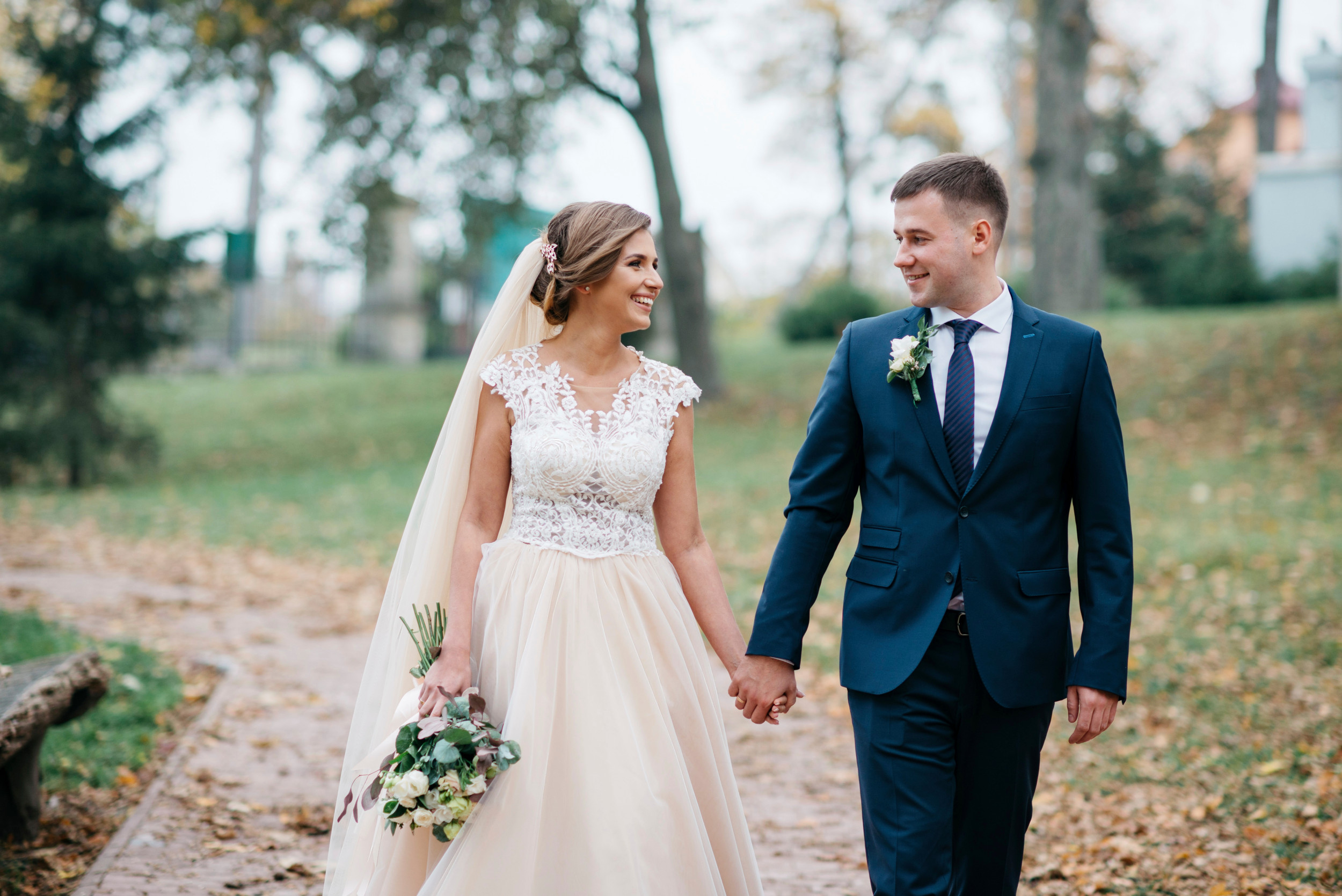 Brudepar går i park med hinanden i hånden og ser forelskede på hinanden.