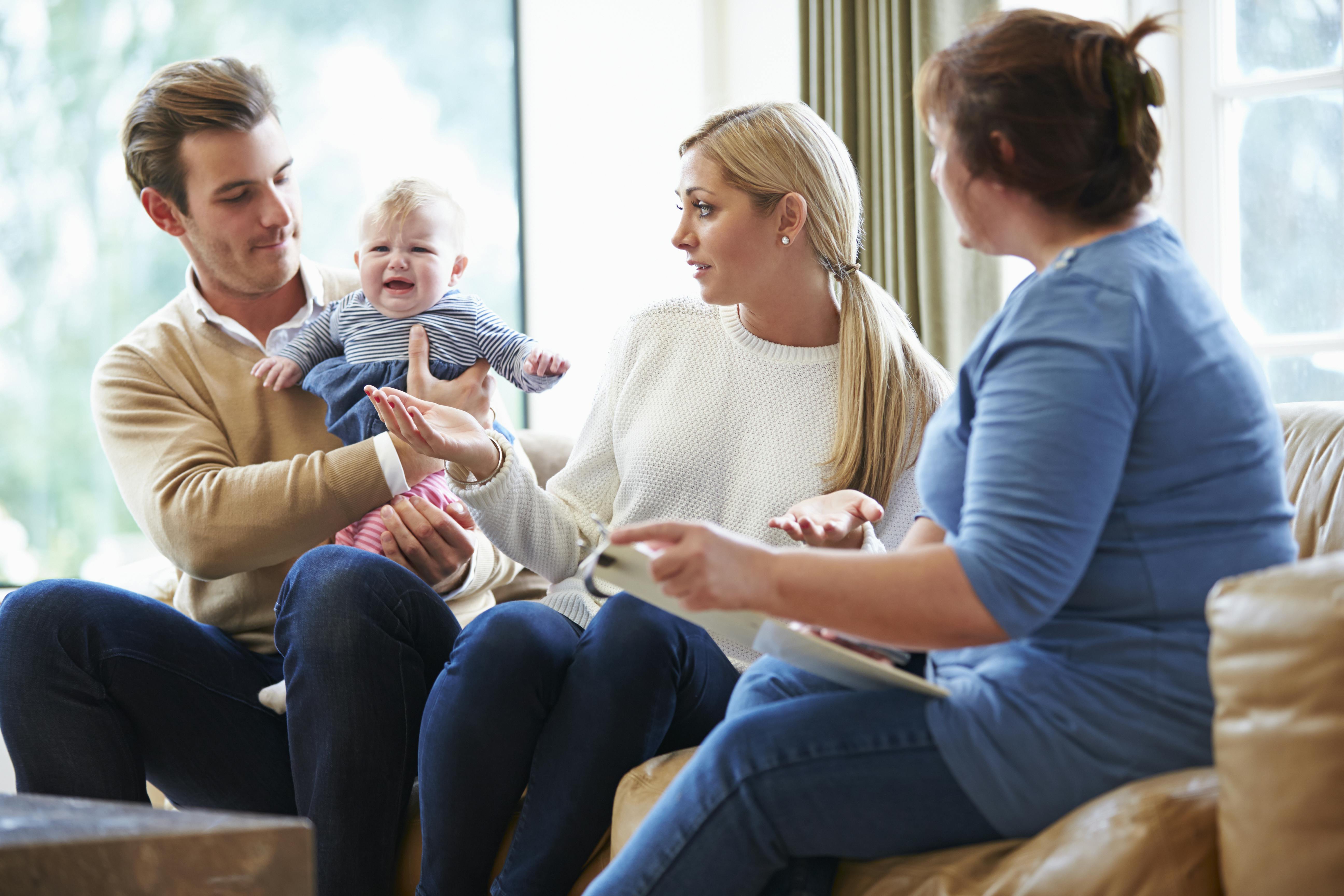 Far holder en lidt utilfreds baby, mens mor og farmor ser på.