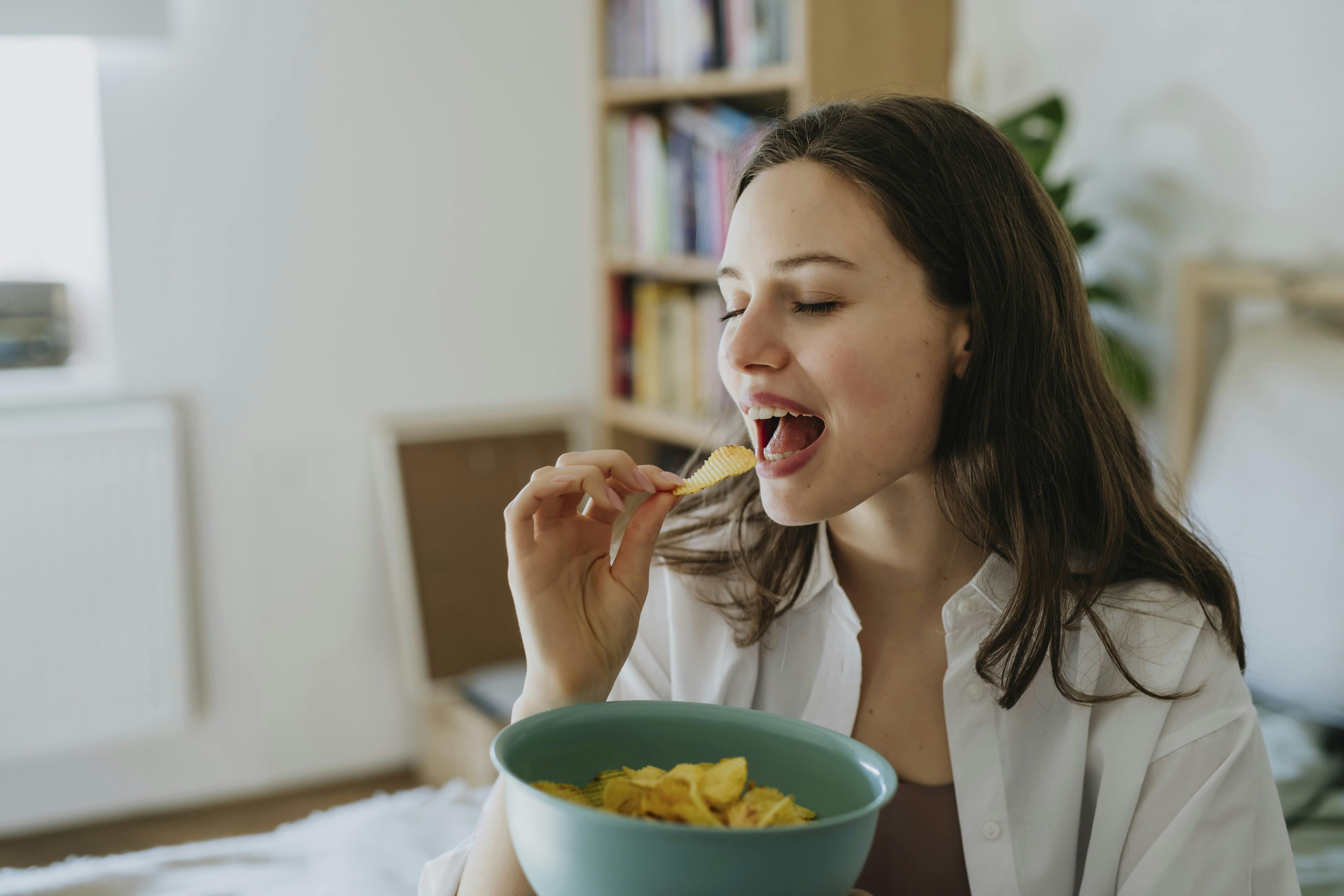 Kvinde der sidder og spiser chips. 