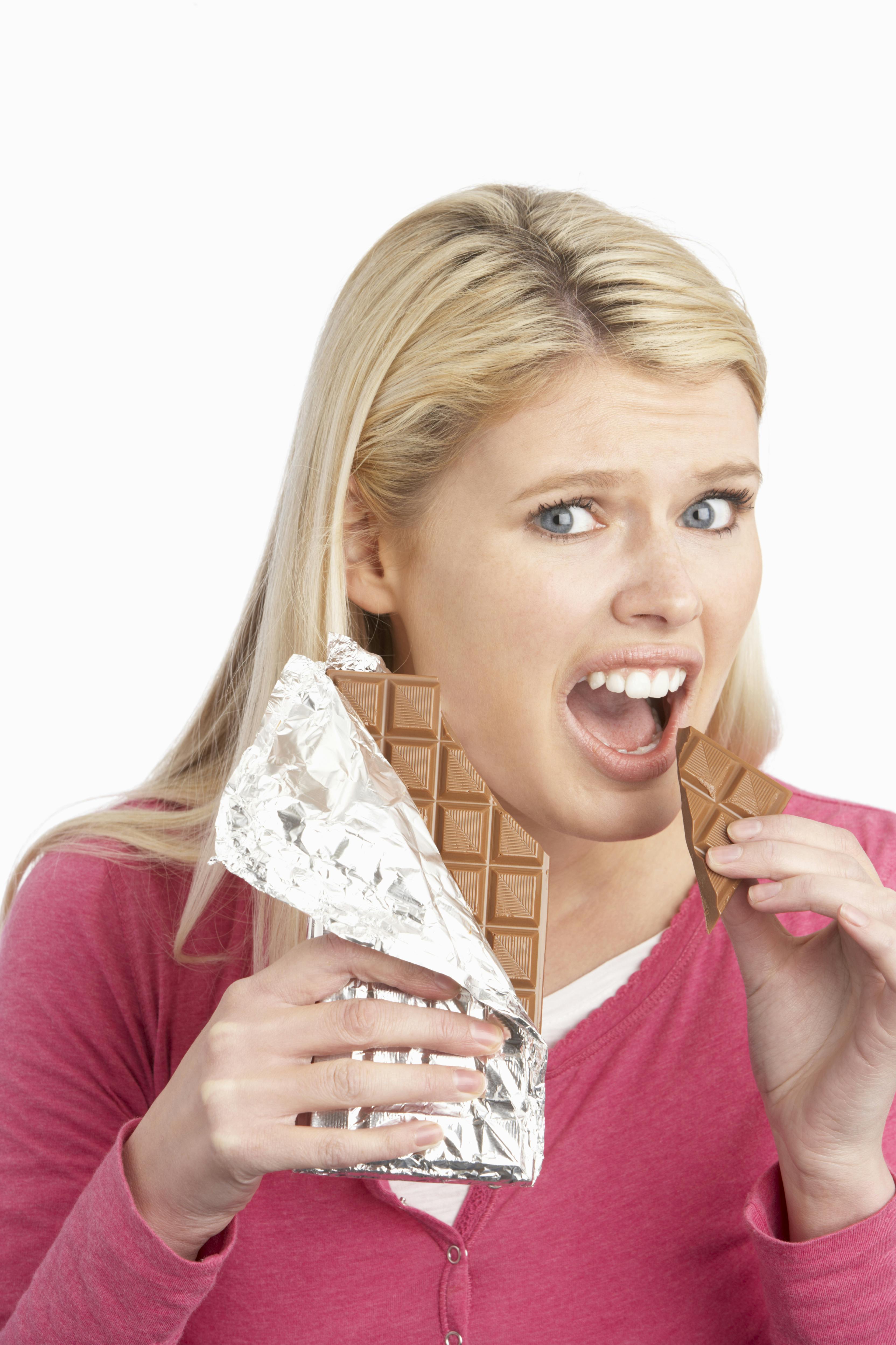 En ung kvinde spiser et stykke chokolade med et skyldigt blik. Hun holder resten af pladen med chokolade i den anden hånd.