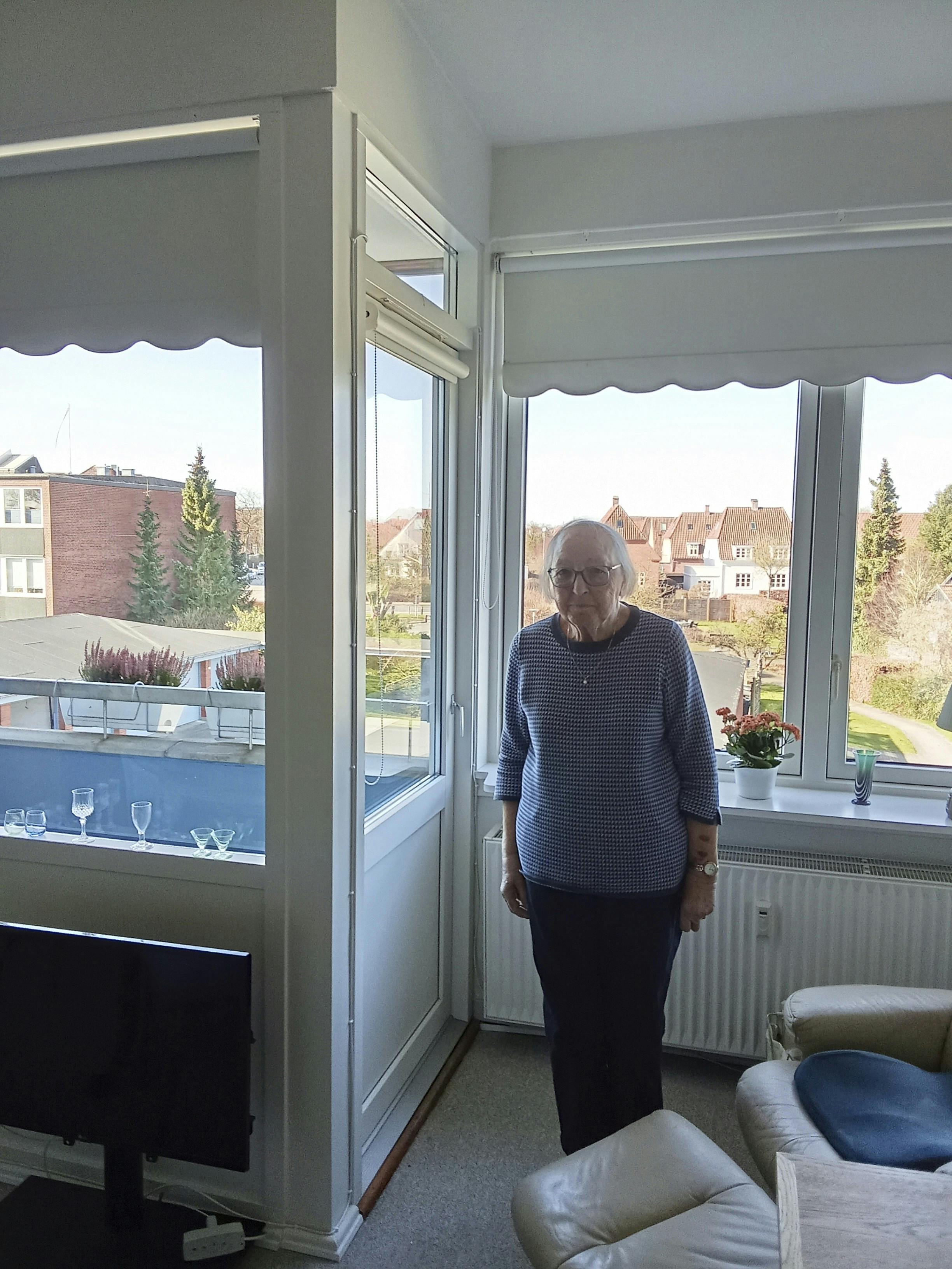 Sonja Milkær der står inde i sin stue, foran et kæmpe vinduesparti. 