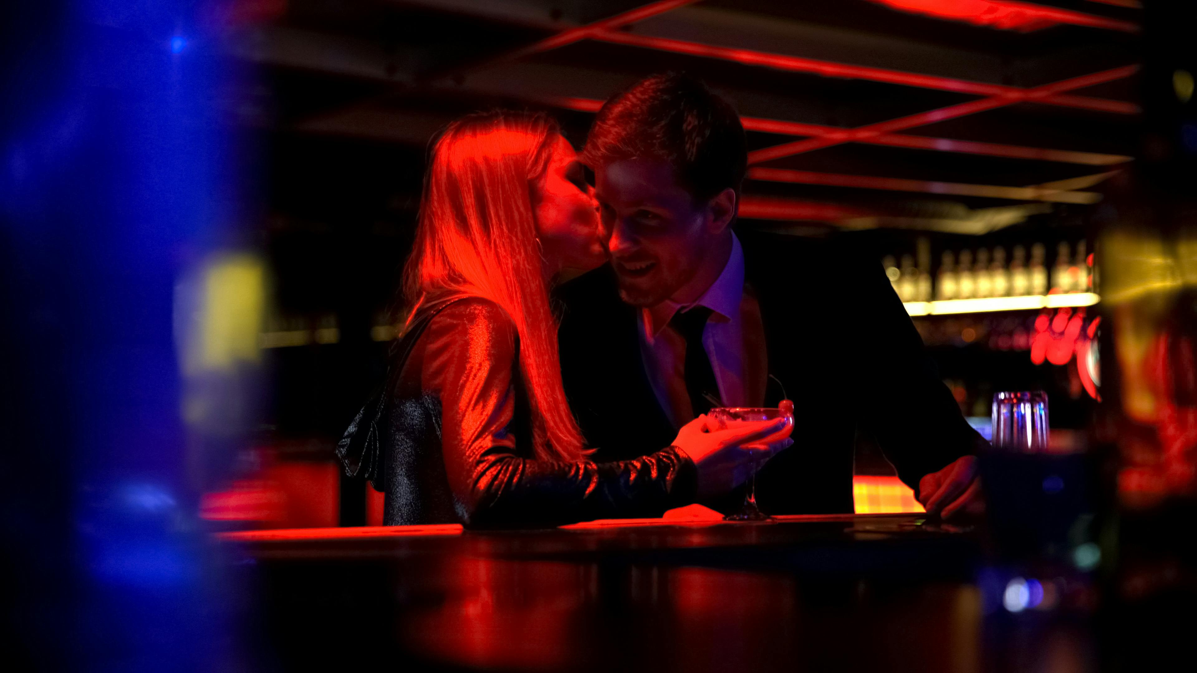 Kvinde kysser flirtende en mand på kinden i en bar.