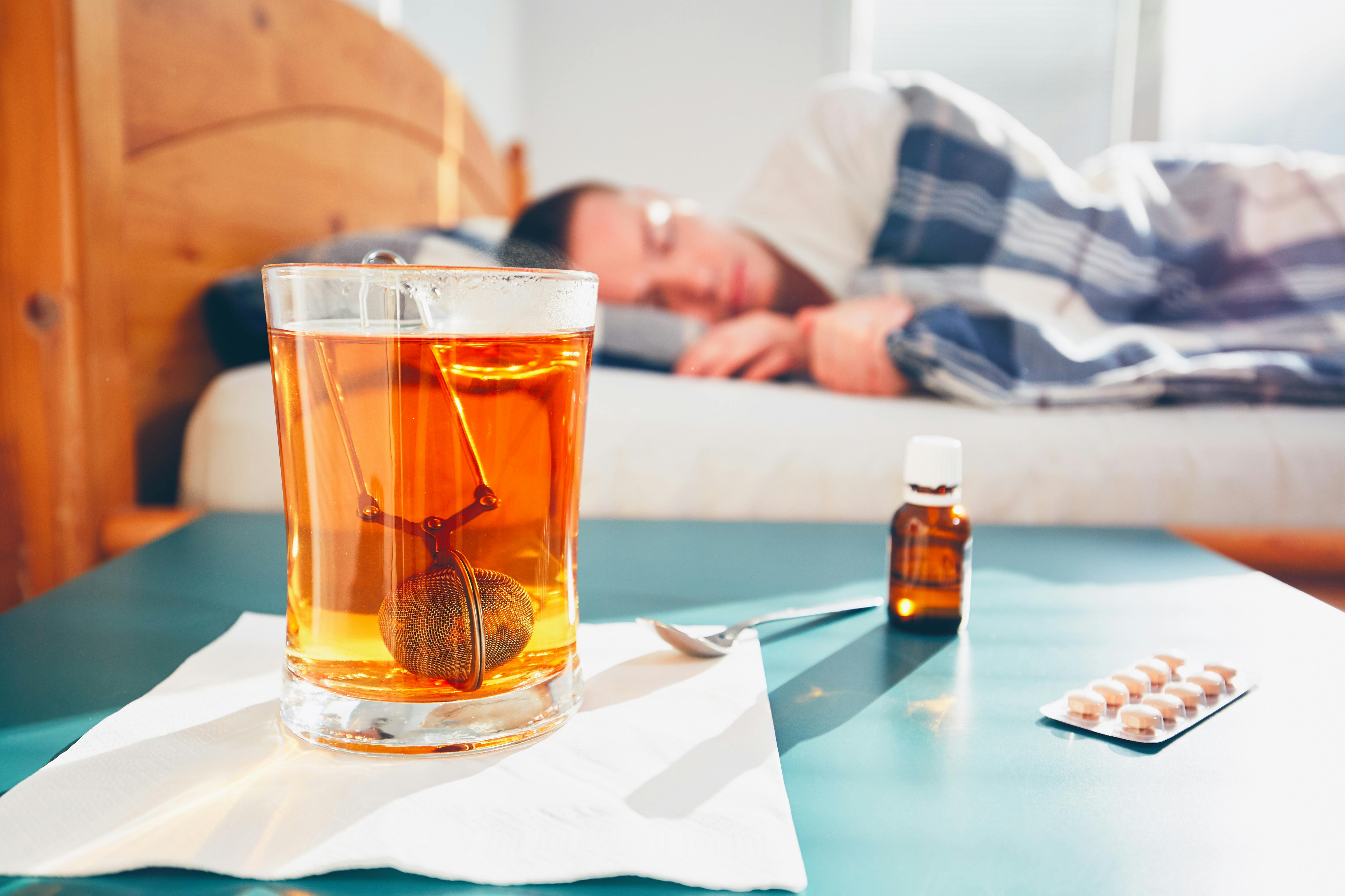 Syg mand ligger i sengen med hostemedicin på sengebordet