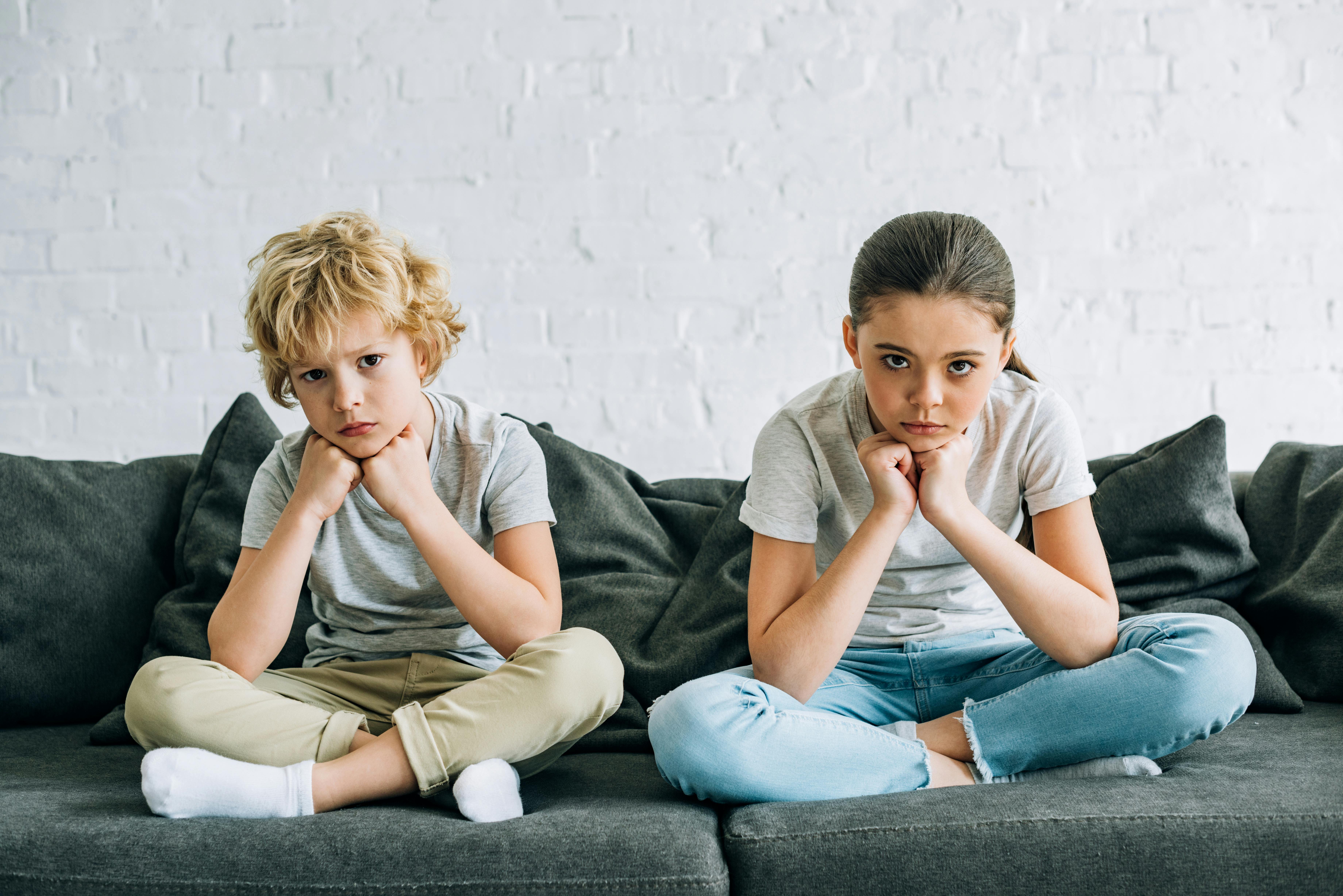Bonusbørn: En dreng og en pige på 8-10 år sidder på en sofa med hænderne knyttet under hagen. De ser triste ud.