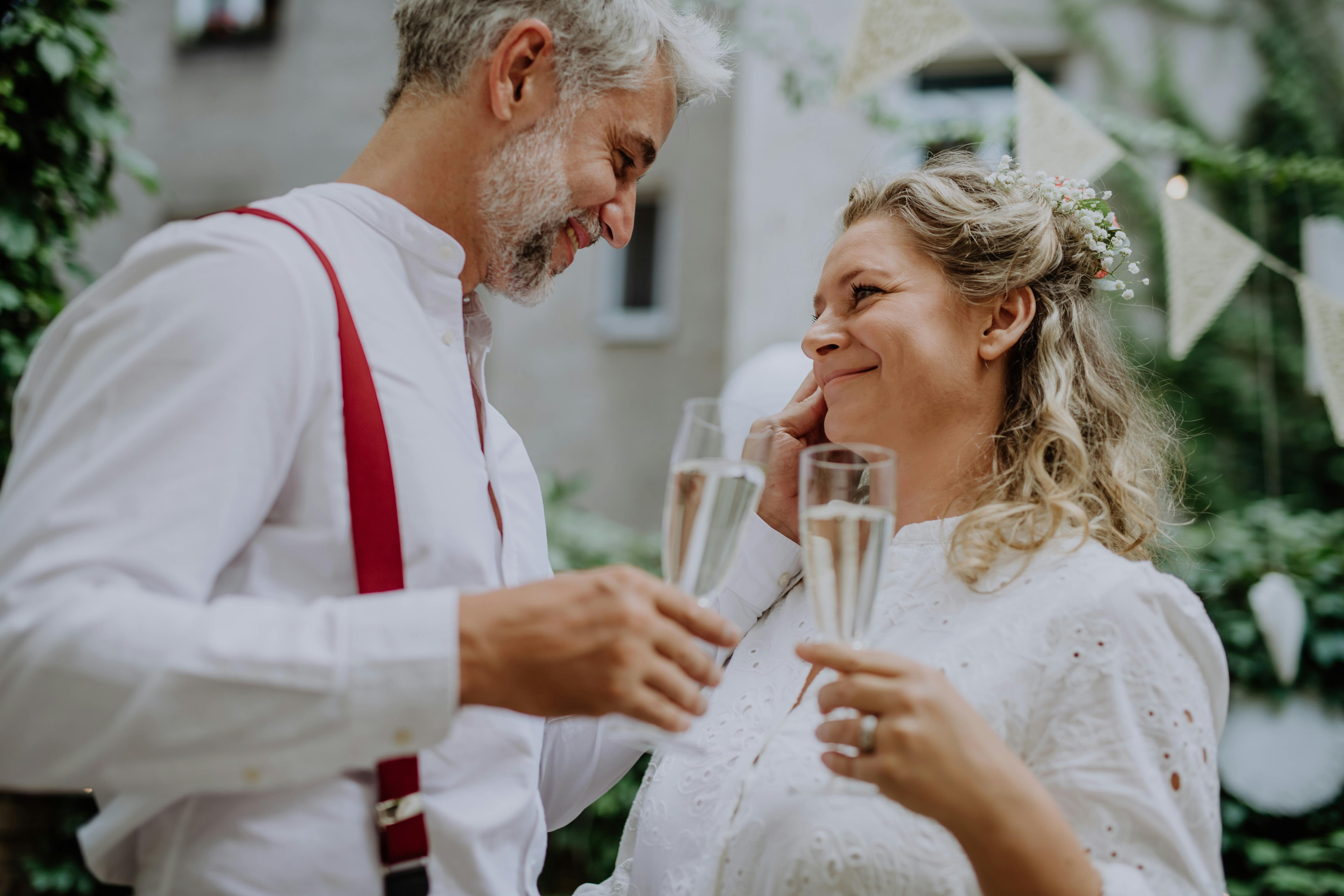 Brudepar står i en have og ser kærligt på hinanden med hvert sit glas champagne i hånden.