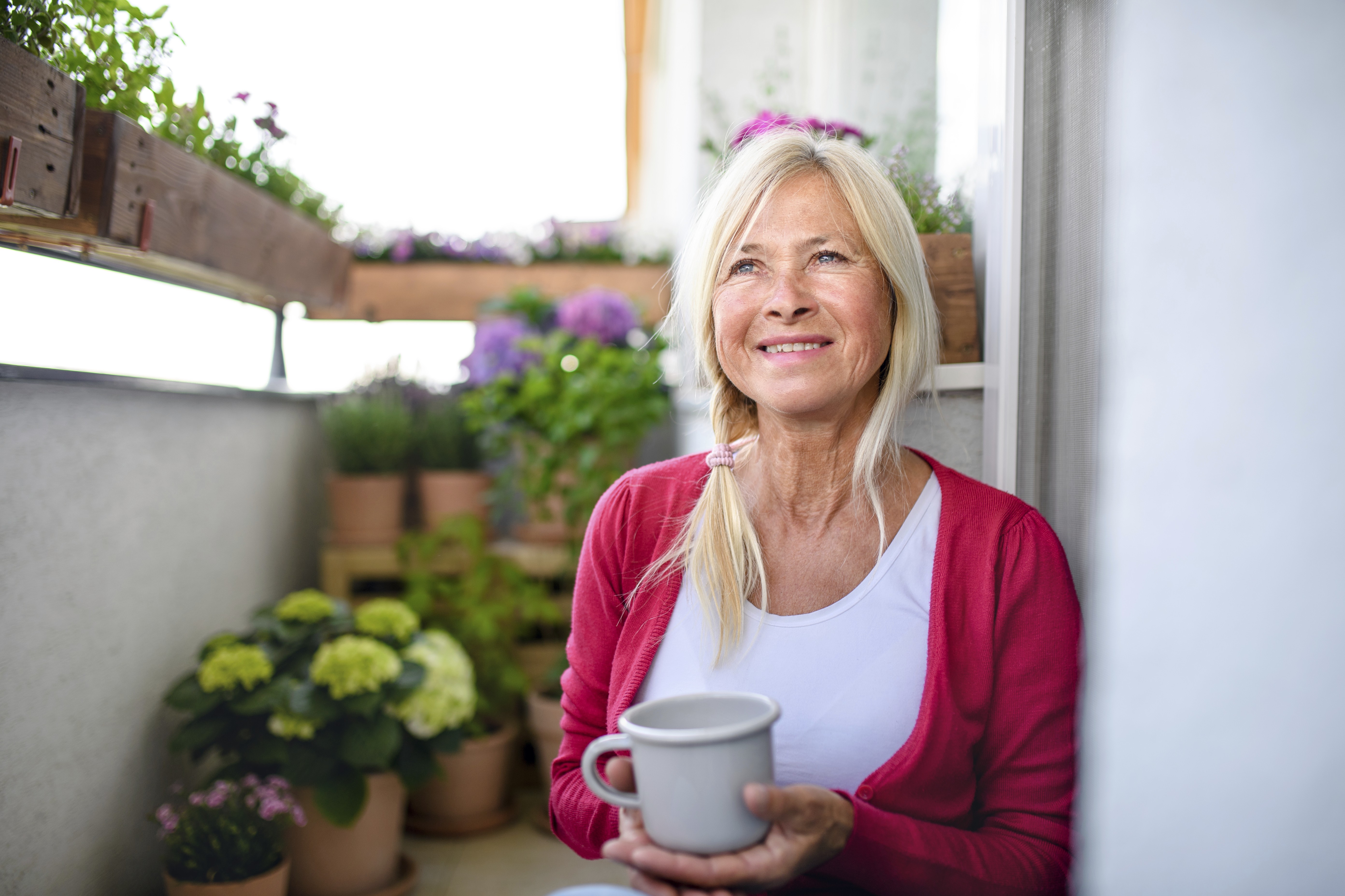Ældre kvinde der sidder på et trappetrin og drikker en kop kaffe. 