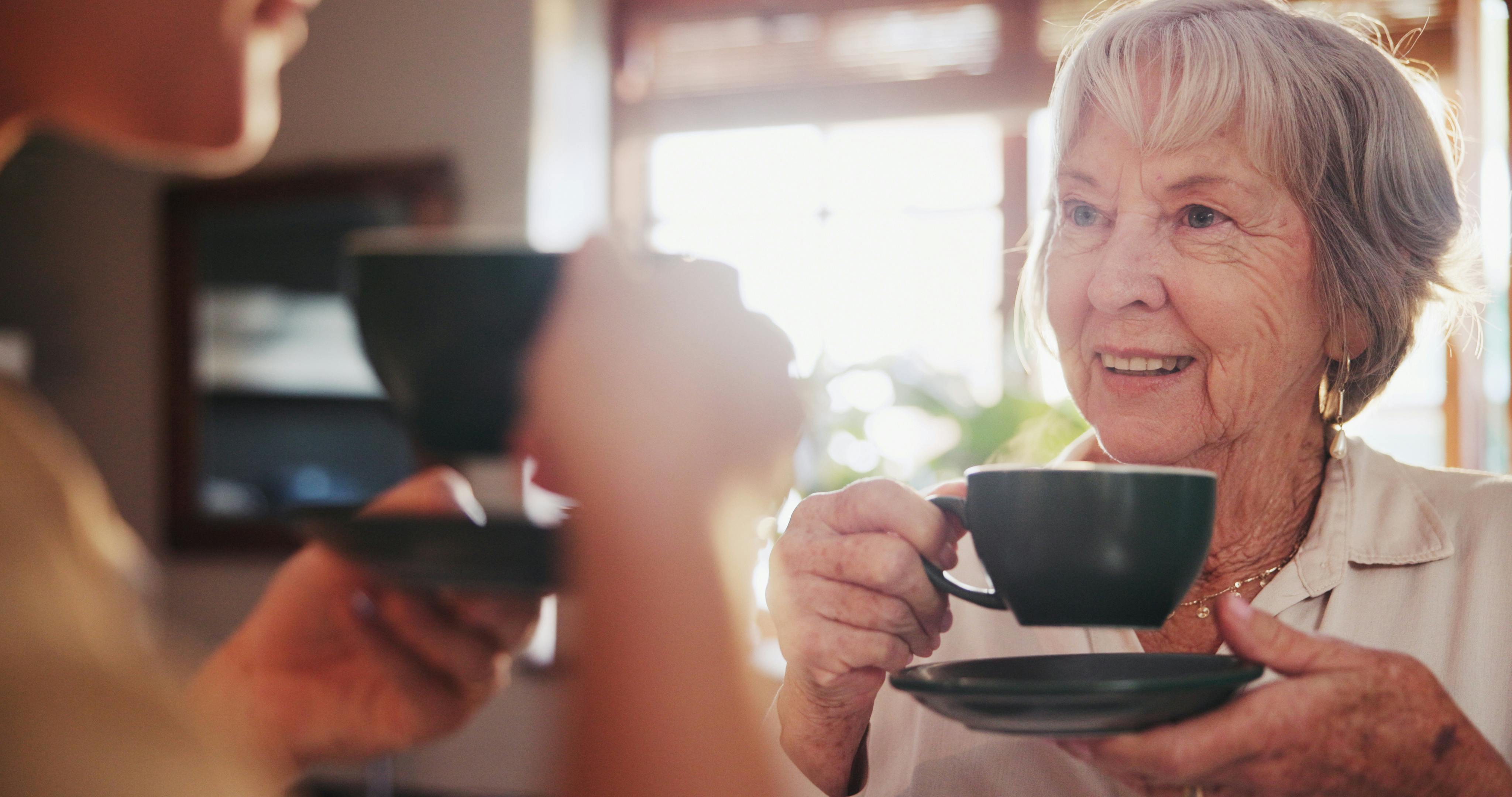 Ældre glad kvinde drikker kaffe i køkken.