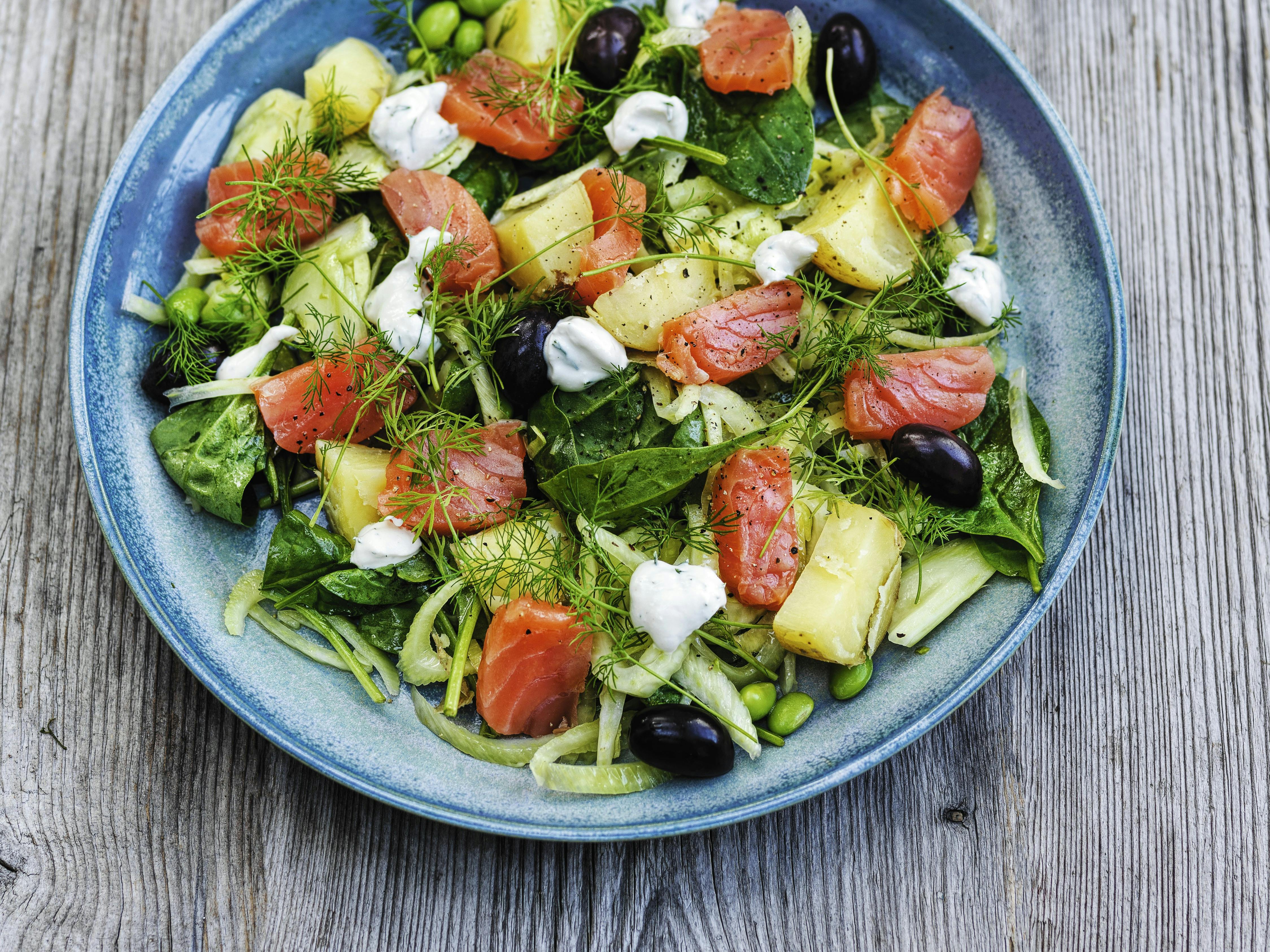 Fennikelsalat med råmarineret laks anrettet på en blå rustik tallerken.