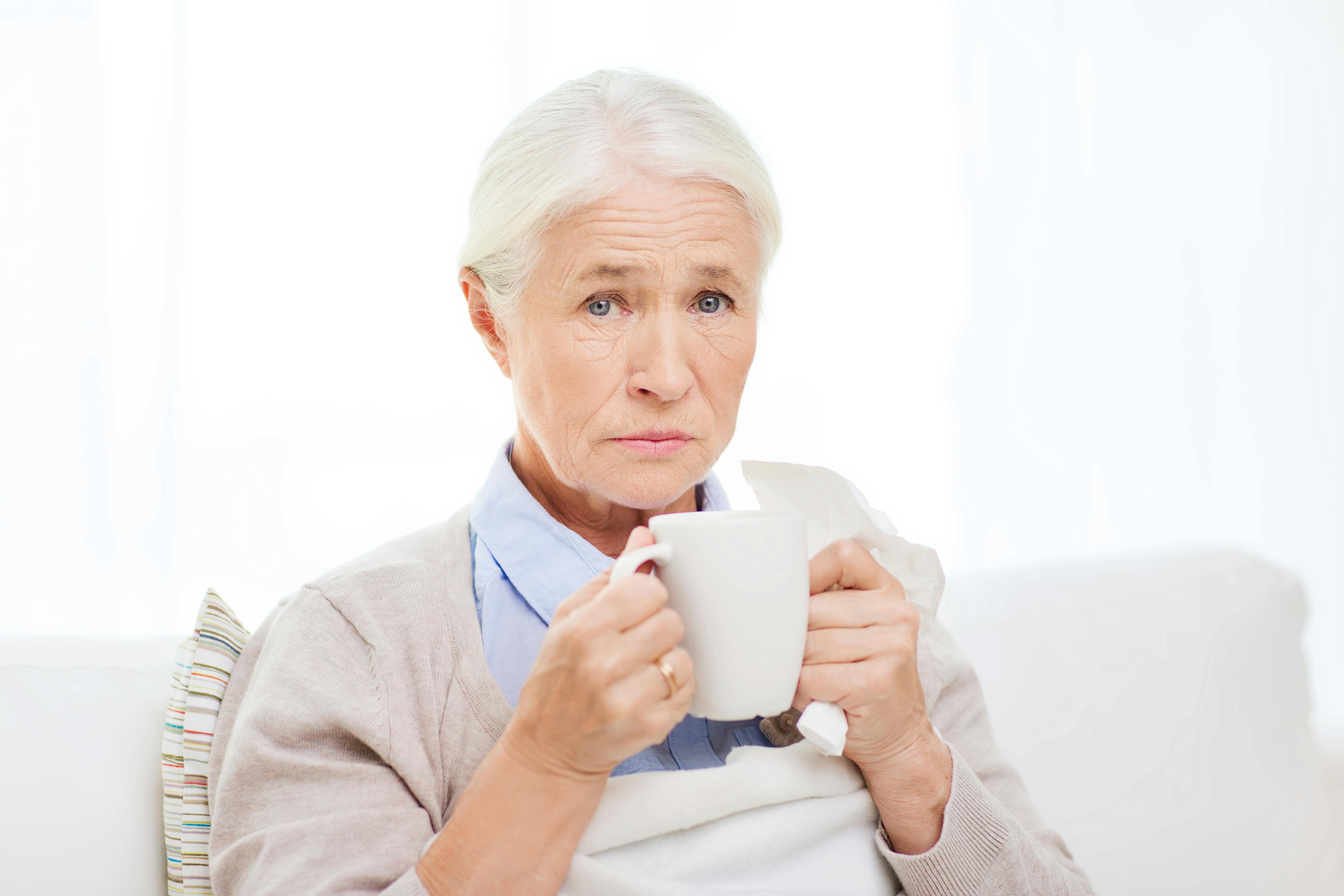 Mormor har slået barnebarn: Ældre kvinde sidder i sofaen med en kop kaffe og ser trist og forladt ud.