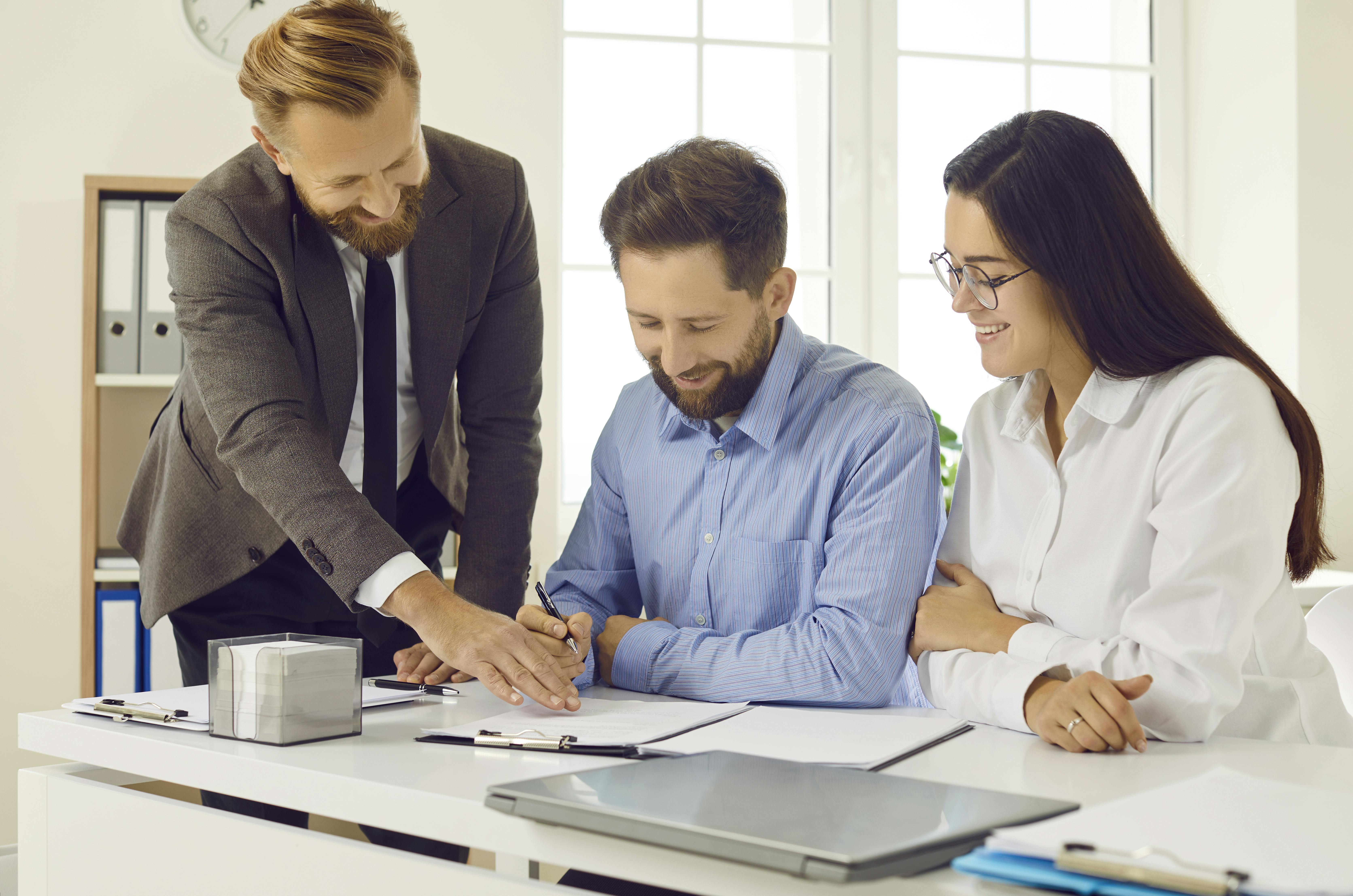 Et par er ved at underskrive papirer, mens deres advokat står ved siden af.