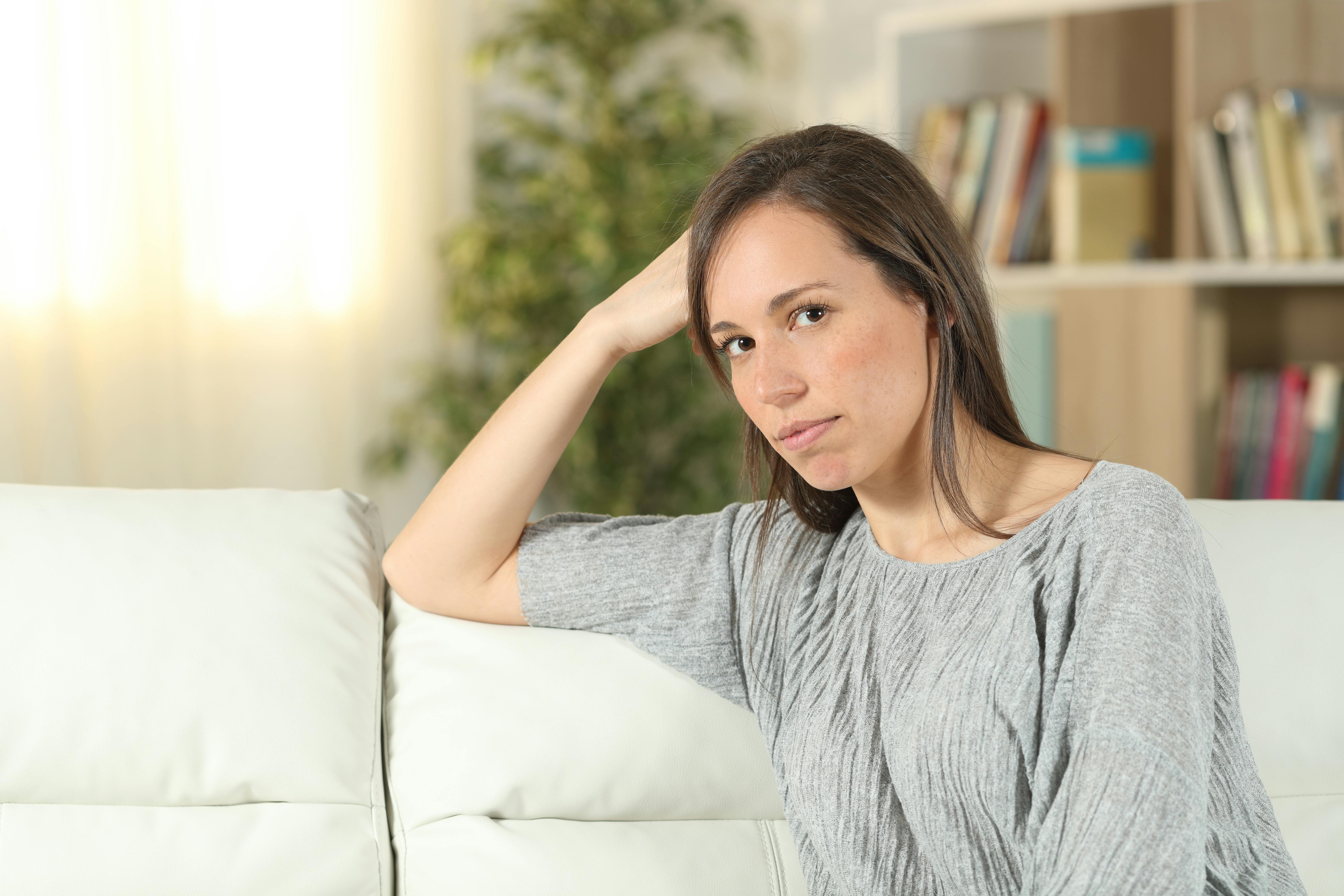 Singleliv og forventingspres: Ung kvinde sidder i sofaen og ser skeptisk ud.