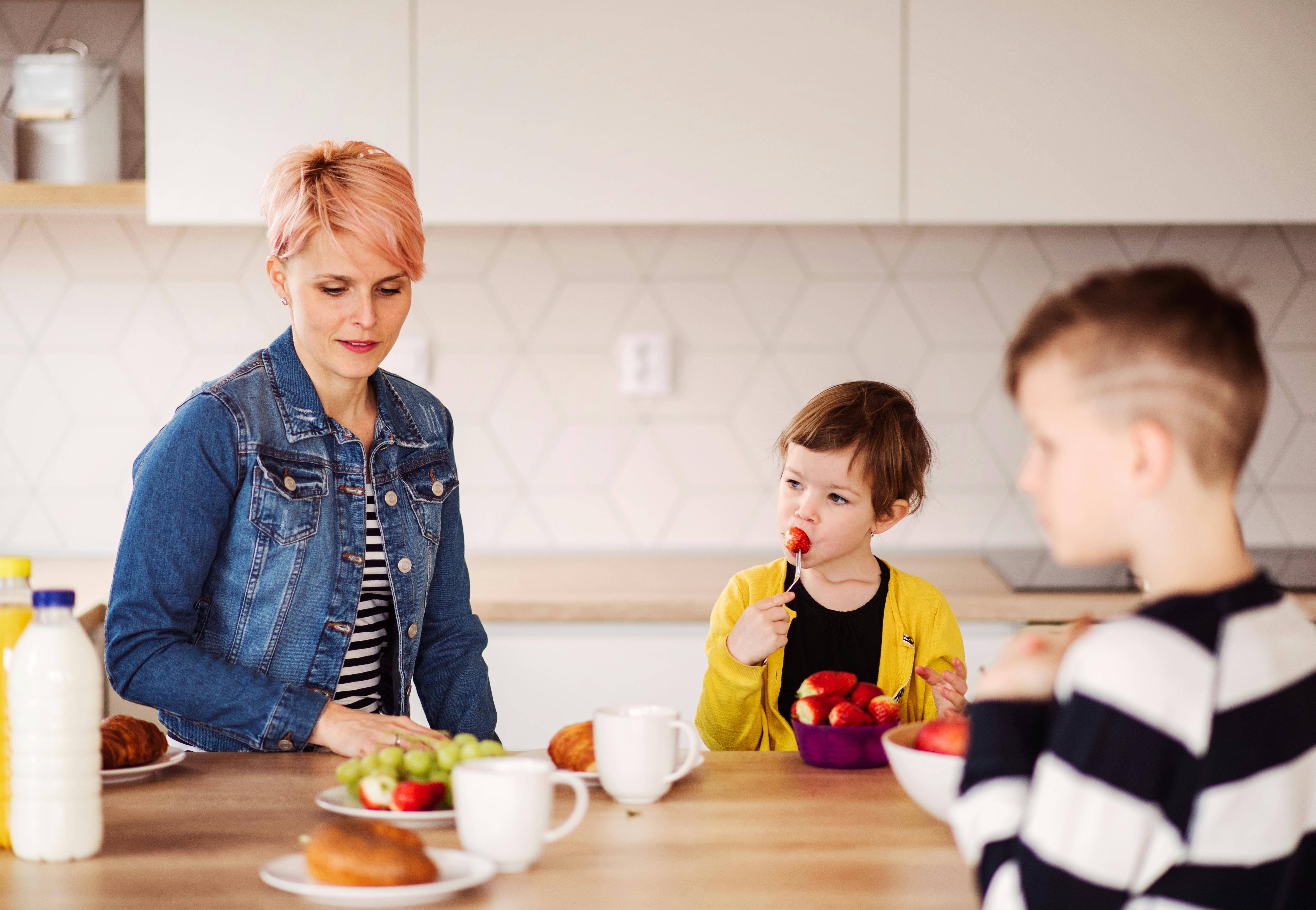 Naboen udnytter mig som barnepige: En mor sidder i køkkenet og spiser frugt med sin datter og naboens søn.
