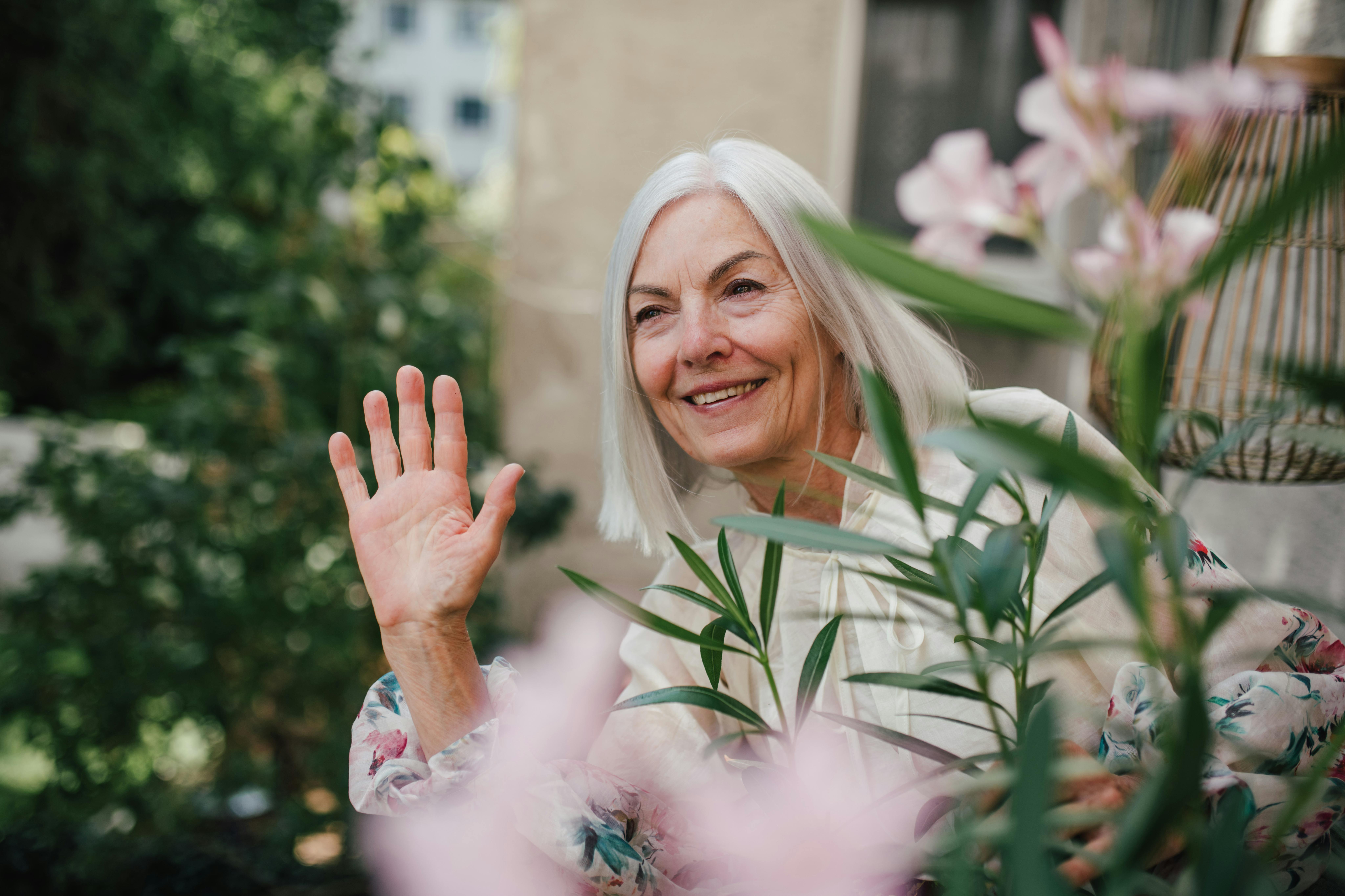 Utroskab: En ældre kvinde står i sin have og vinker glad til naboen.