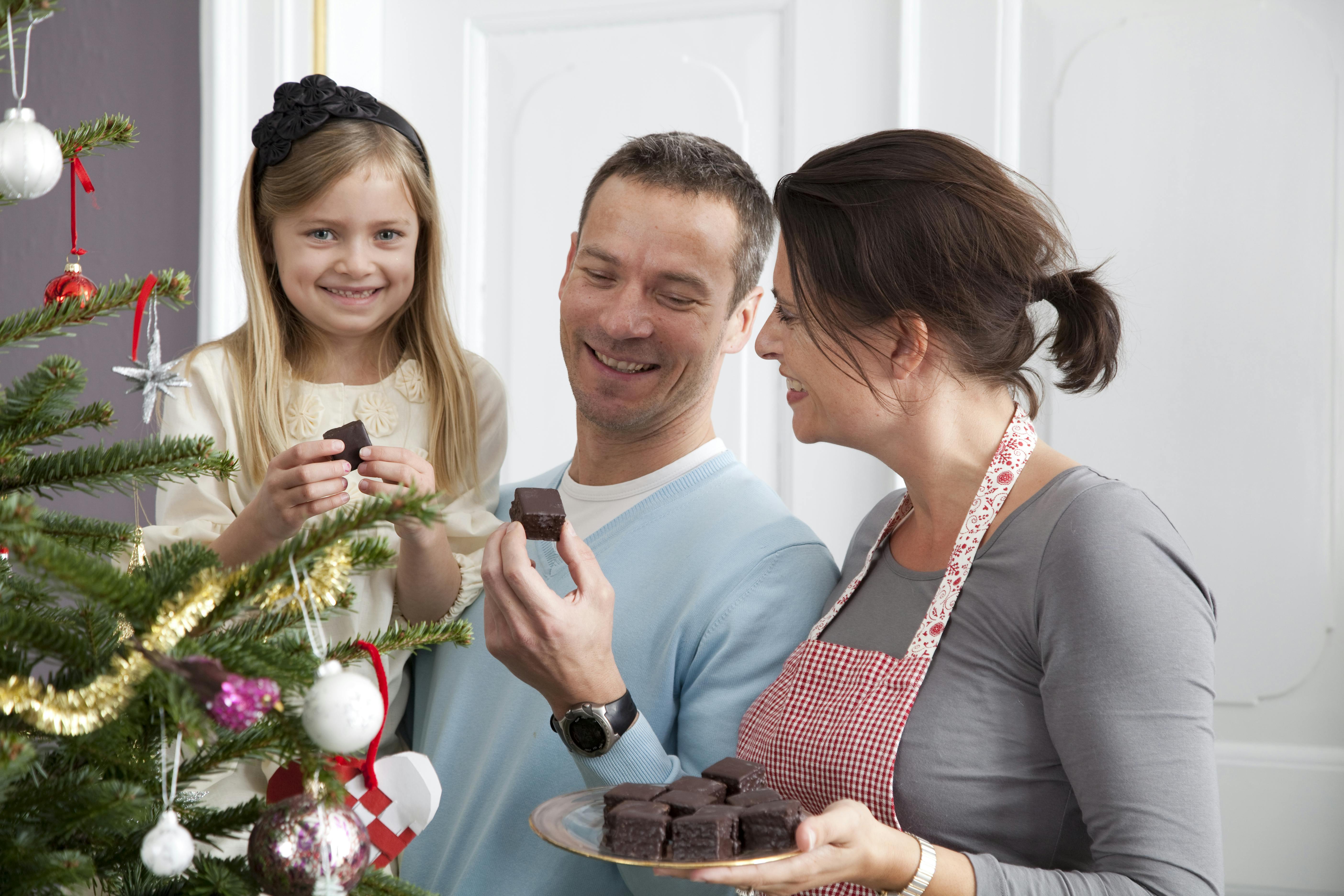 En kvinde serverer konfekt til en mand og en pige, og familien står ved et juletræ.