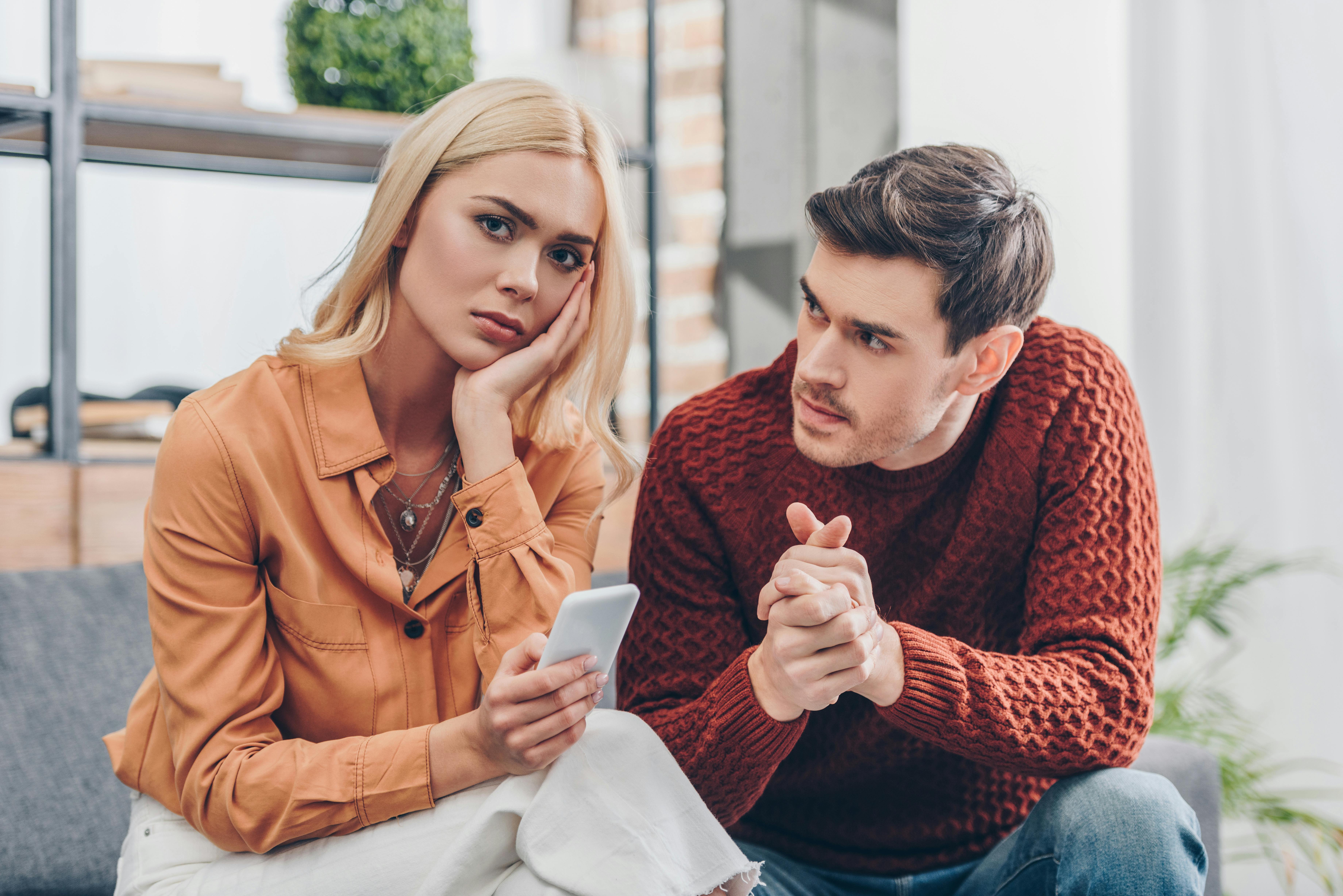 En kvinde vender sig vredt væk fra sin kæreste, der ser appellerende på hende, mens han vrider sine hænder.