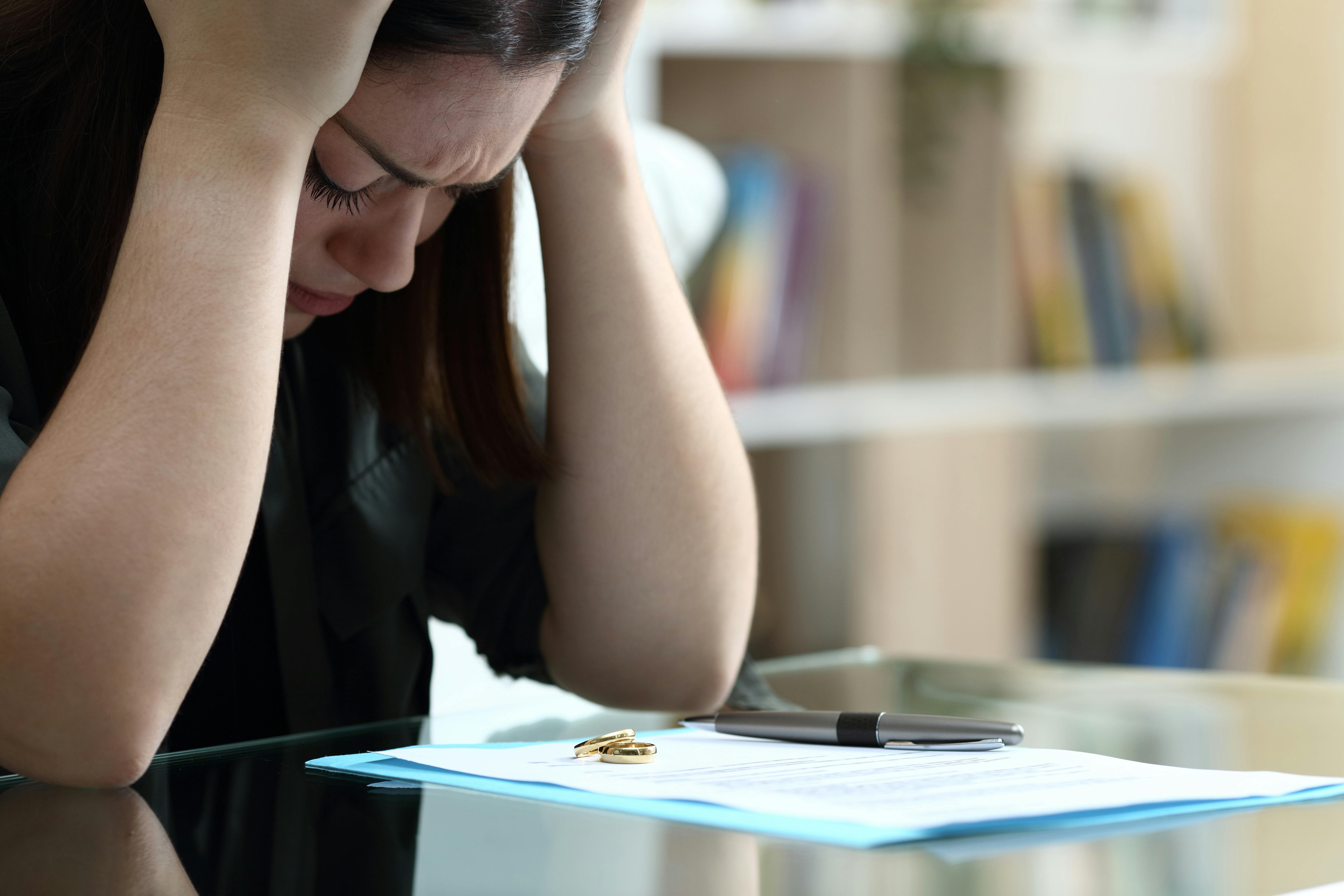 Skilsmisse: En kvinde tager sig fortvivlet til hovedet, mens hun sidder foran nogle dokumenter, hvor der også ligger en vielsesring.