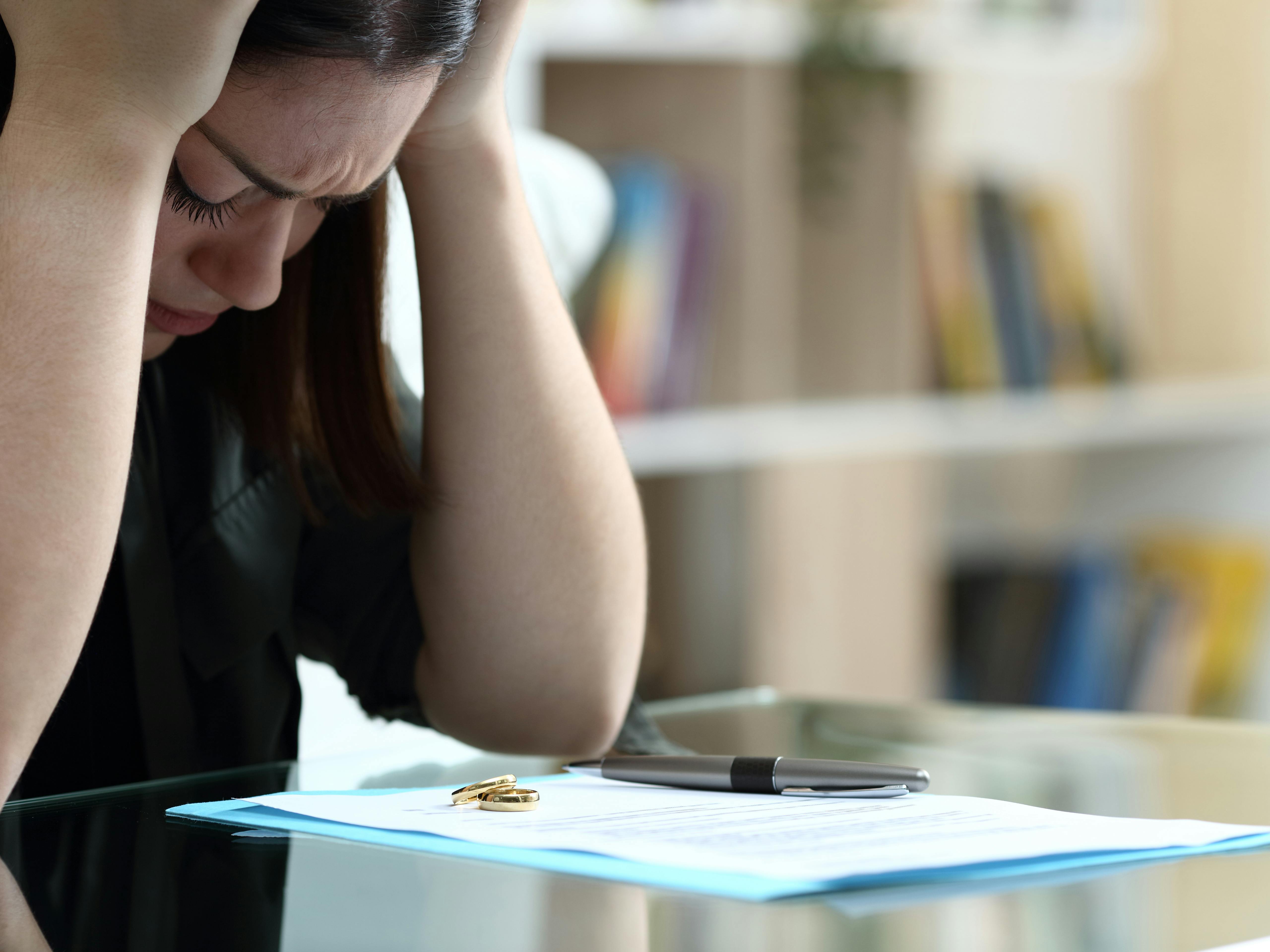 Skilsmisse og bodeling: Snydt af eksmanden - En kvinde tager sig fortvivlet til hovedet, mens hun sidder foran nogle dokumenter, hvor der også ligger en vielsesring.