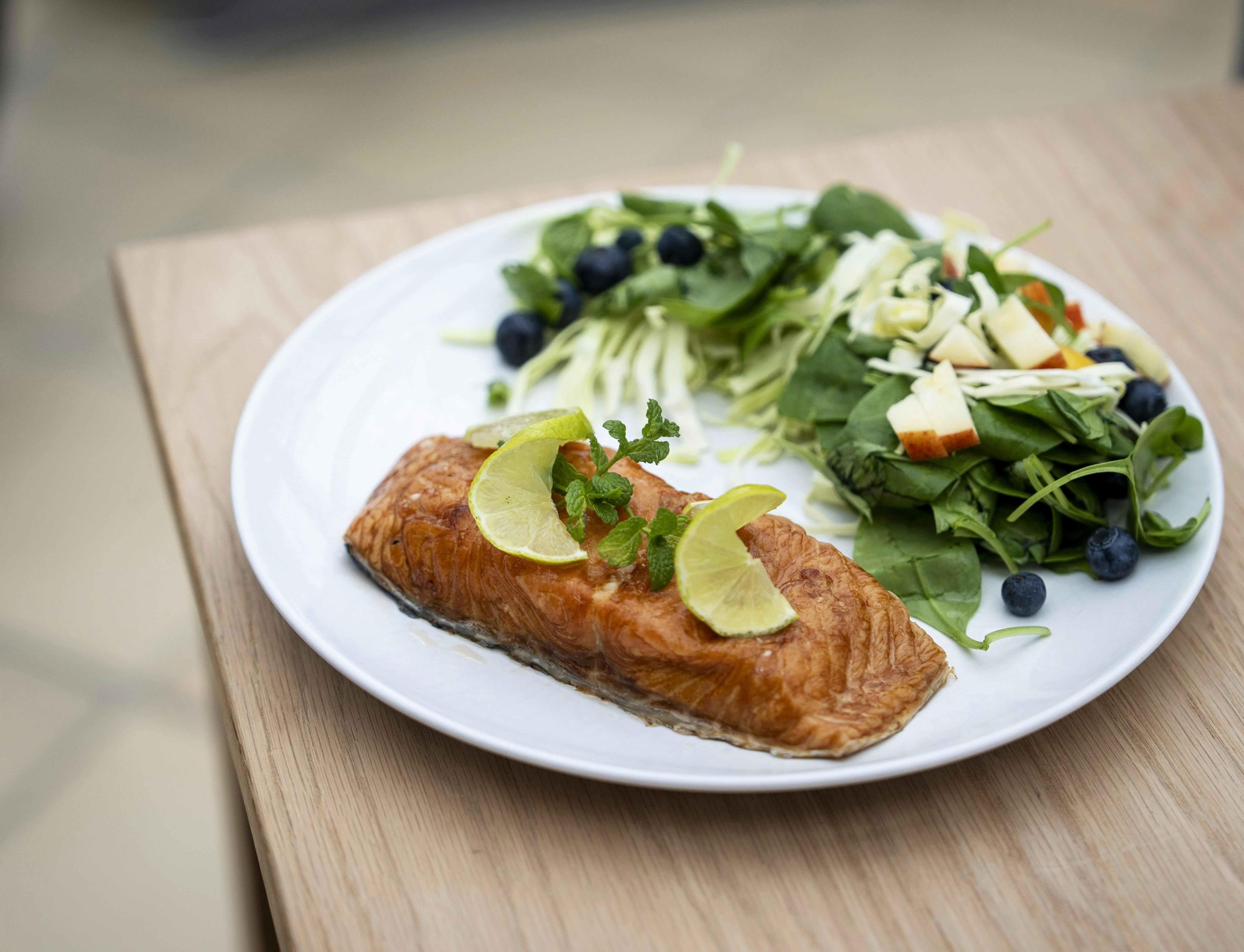 En tallerken med et stykke laks pyntet med citronskiver og grøn salat.