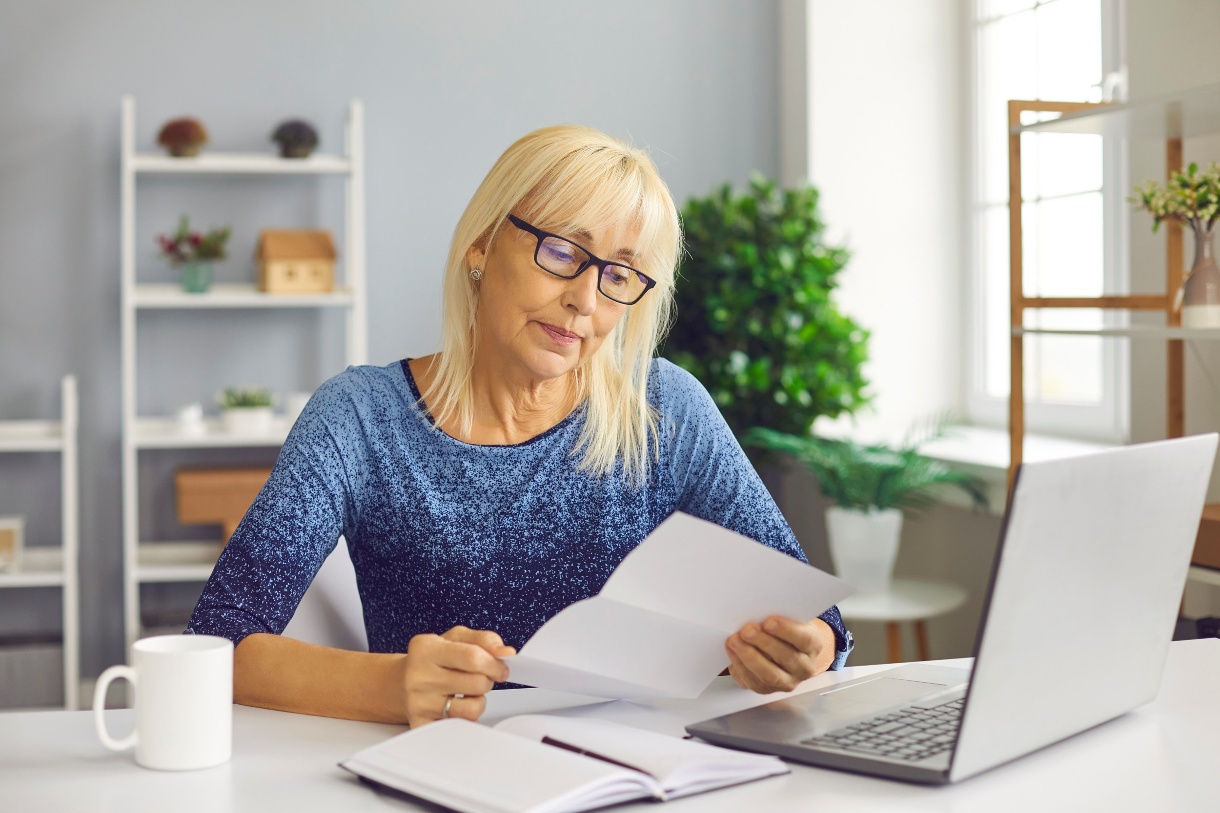 Midaldrende kvinde sidder ved sit spisebord og læser et brev.