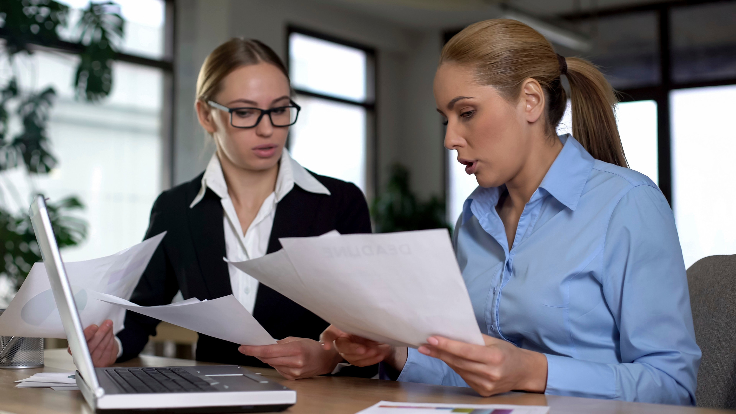 Kvindelig chef ser misbilligende på sin medarbejde, der sidder med nogle papirer.