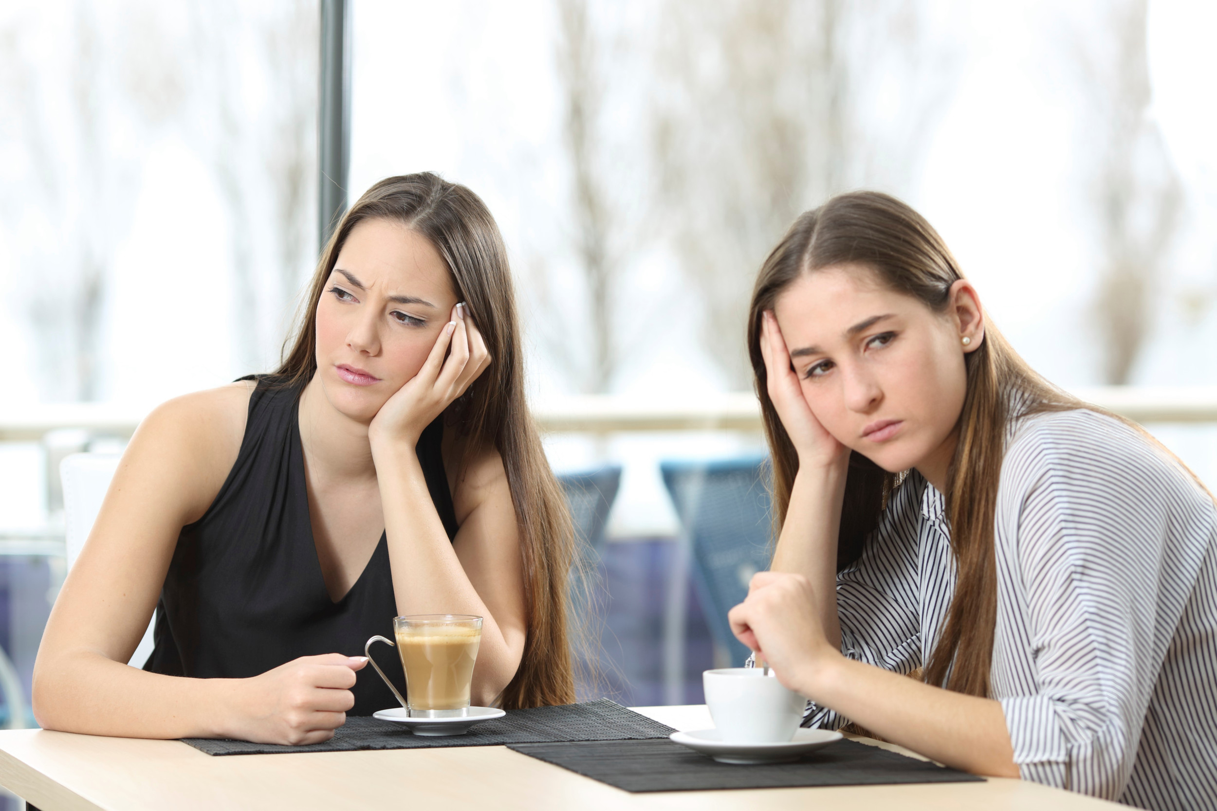 To veninder sidder på en café med en kop kaffe og ser surt i hver sin retning.