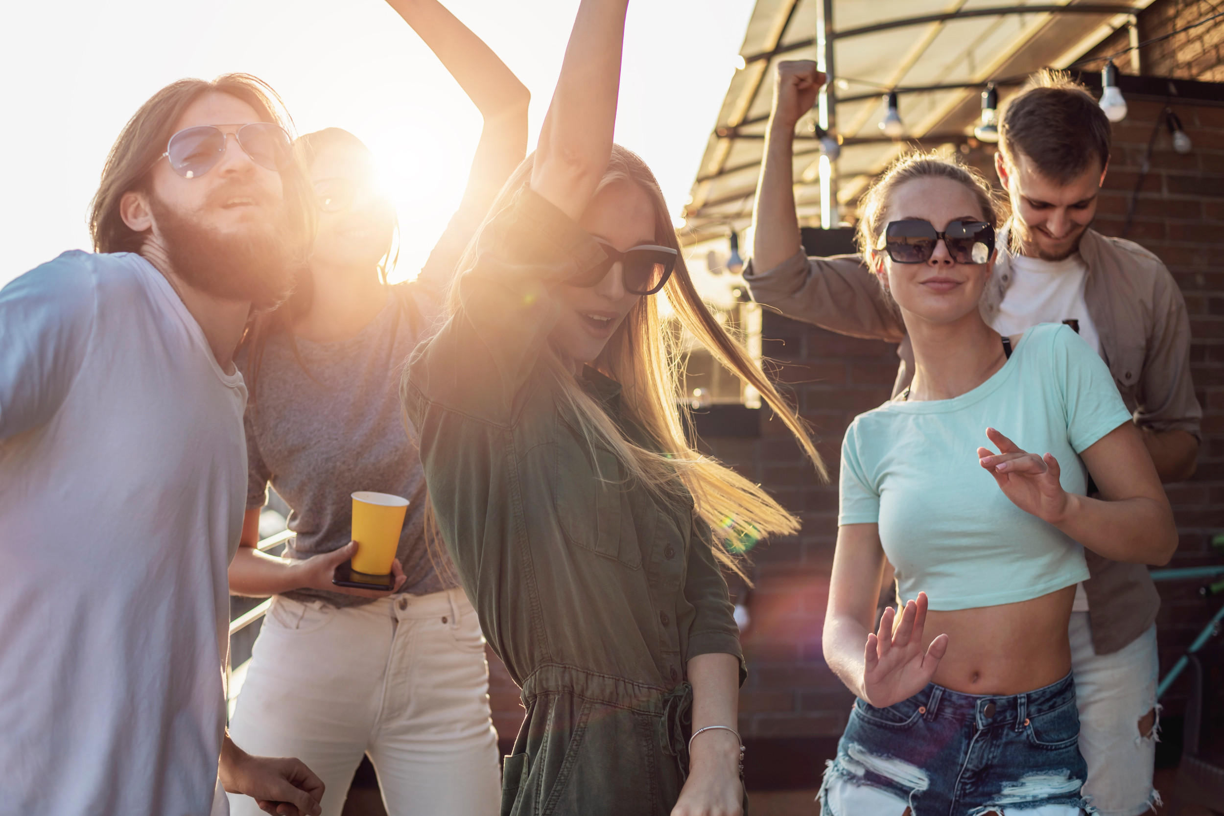 En flok glade, unge mennesker står på en altan og danser og fester.