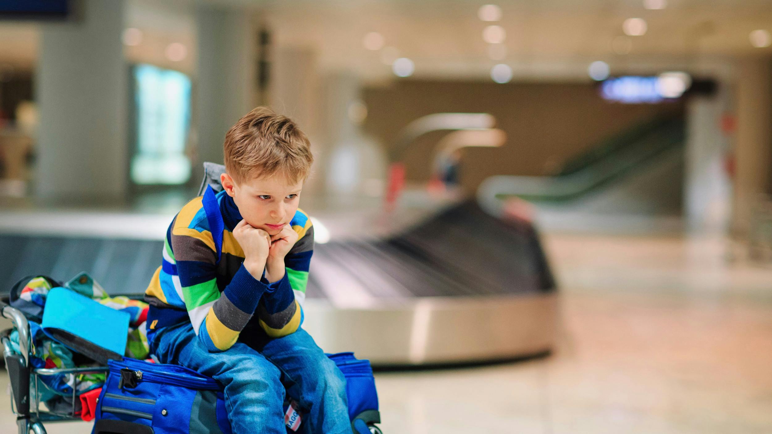 Lille dreng sidder på sin bagage i lufthavnen