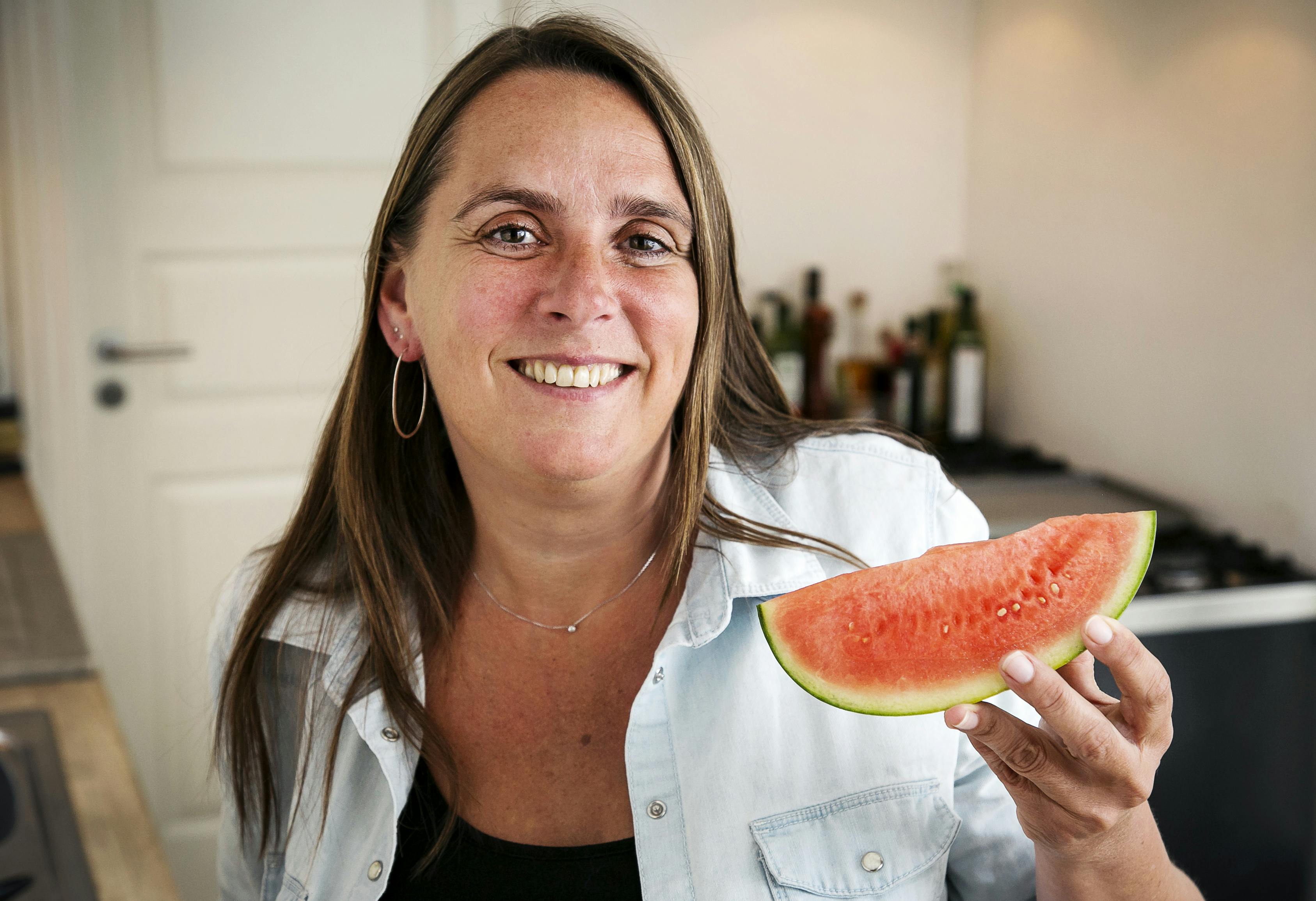 Anne Hjernøe står med en melonskive i hånden i sit køkken 