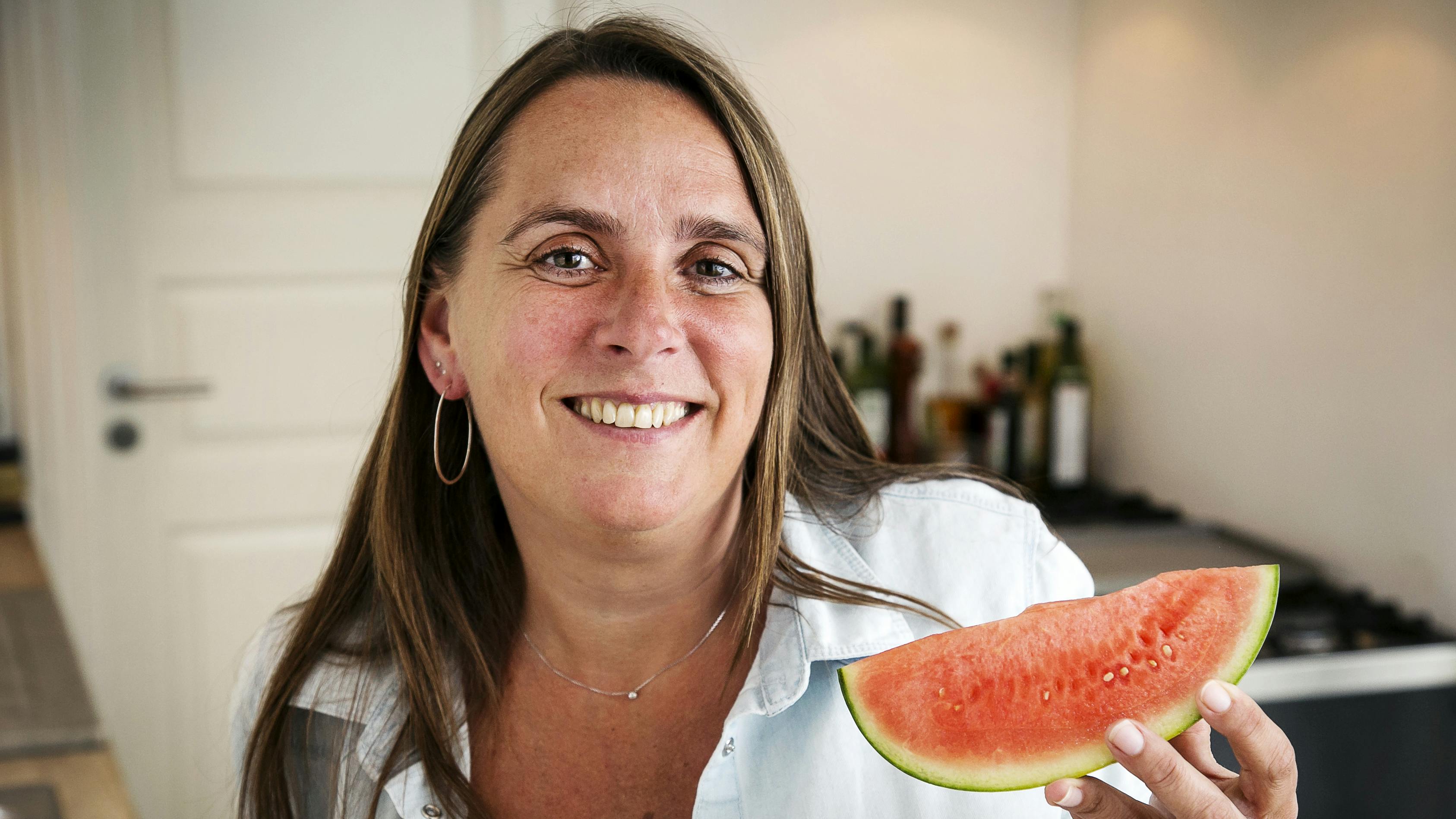 Anne Hjernøe står med en melonskive i hånden i sit køkken 
