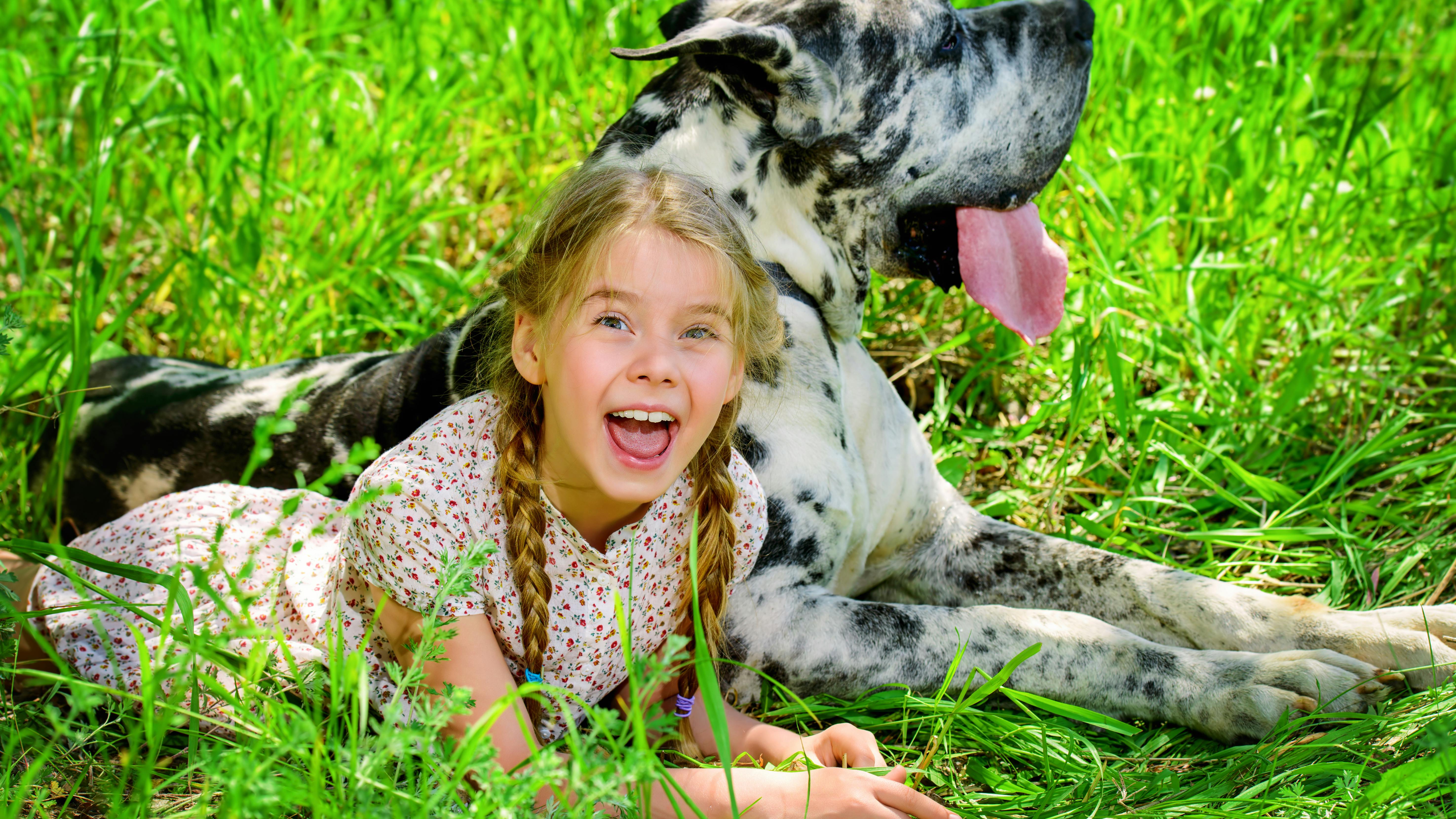 En pige og hund ligger i græsset