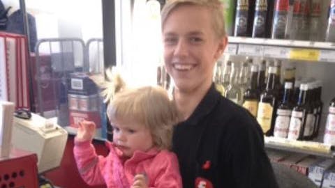 En lille ny medarbejder i Fakta. Kassemedarbejder 17-årige Søren Mikkelsen har taget lille Penny op på skødet, så hun kan være med til at scanne varer. 