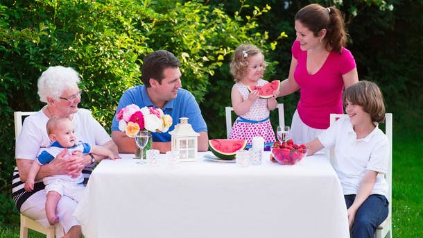 Familie sidder udenfor samlet om et bord og spiser middag