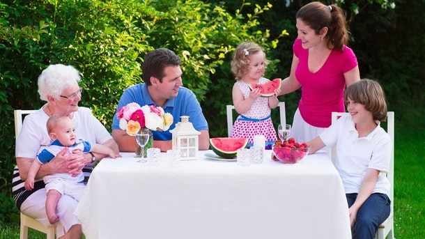 Familie sidder udenfor samlet om et bord og spiser middag